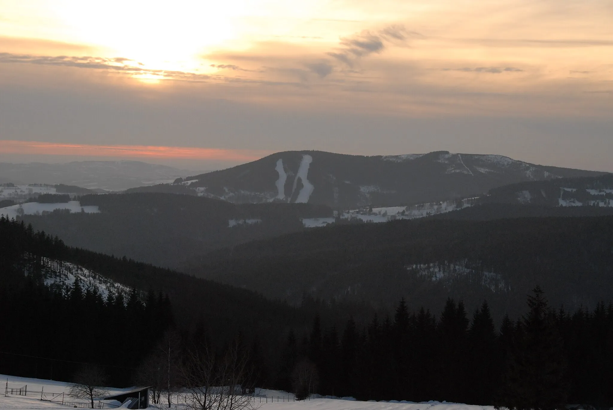 Photo showing: Pohled od Tetřevích bud na Přední Žalý (1018 m.n.m.) a tamější herlíkovické sjezdovky, vedle něho Zadní Žalý (1035 m.n.m.), před nimi Strážná hůra (824 m.n.m.), Strážné a kousek Herlíkovického Žalý (958 m.n.m.), přes údolí naproti vrch o výšce 889 m.n.m.