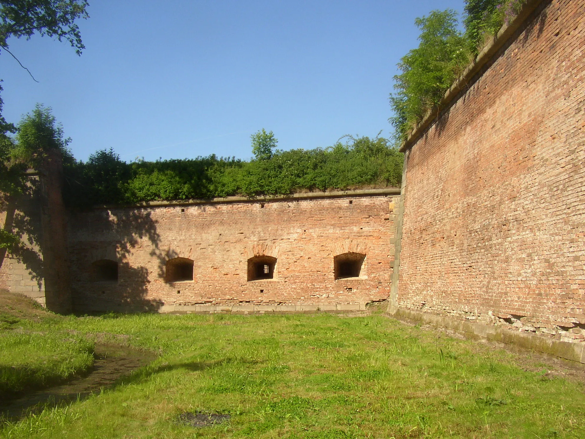 Photo showing: A small example of extensive fortification of Terezín, in this instance from western side of the fortress. Artillery casemates providing cover to the right flank of Ravelin XVIII as seen from bottom of the moat (the escarpe of the ravelin is visible in the right.