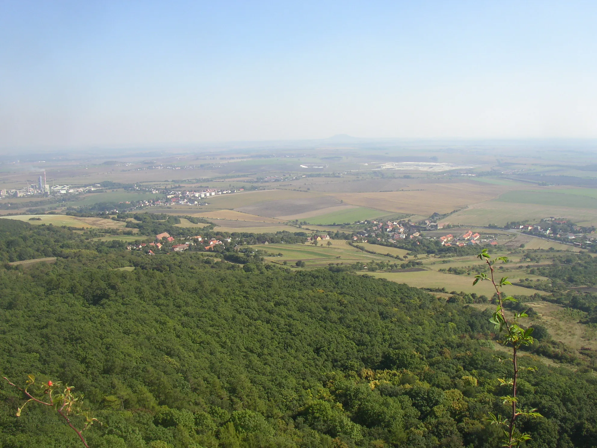 Photo showing: A view from Košťál hill in České středohoří Mts. towards SE. In the right village of Jenčice, in the upper left corner Čížkovice cement works and village of Čížkovice.