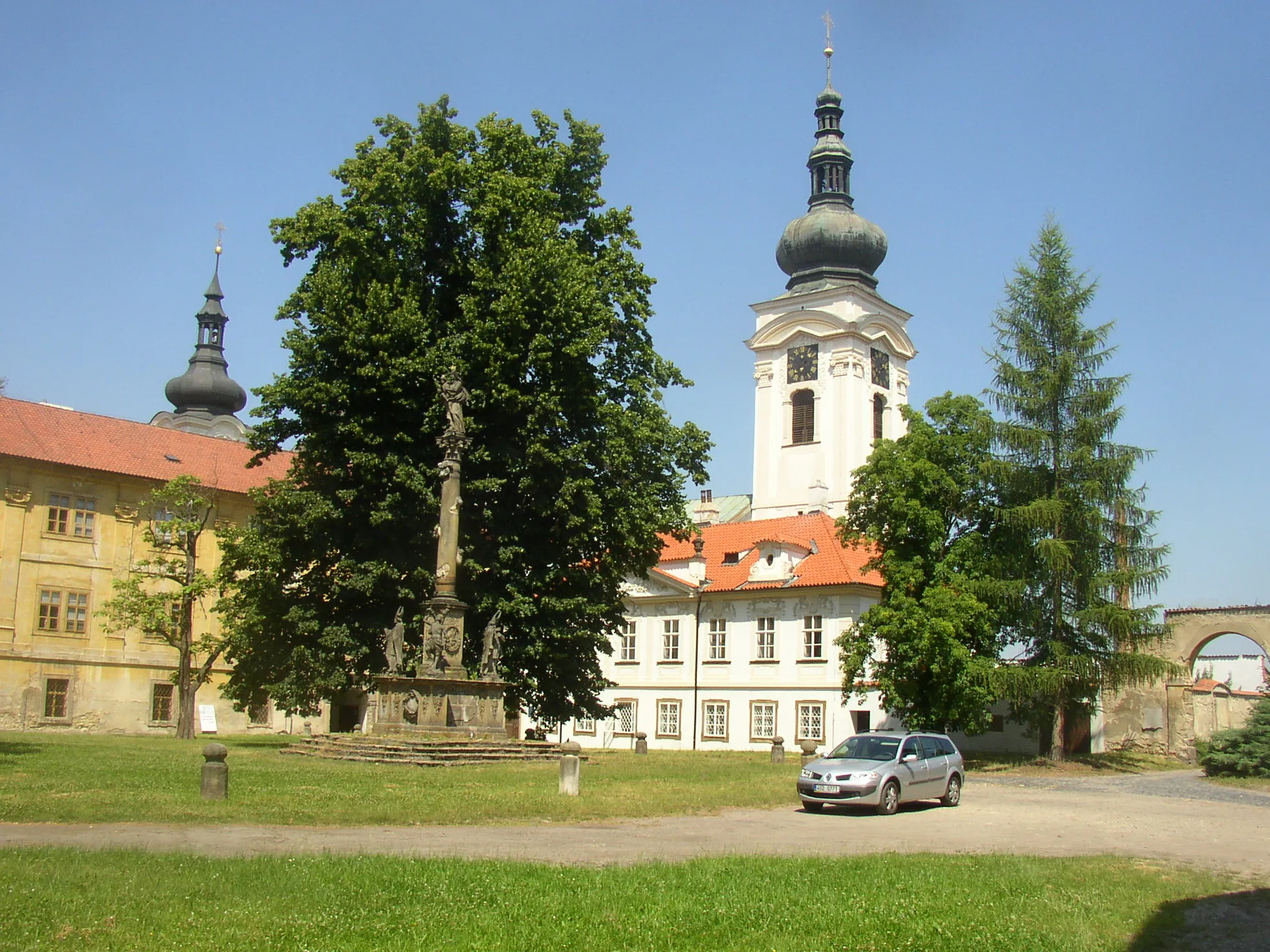 Photo showing: First courtyard of female Premonstratensian convent in Doksany, Litoměřice District, Czech Republic. A view from the southeast, in the middle Marian plague column (1684), in the left building of prelature (1692) separating the first courtyard from the second one, in the right building of provisory (1725-30) with eastern tower (1718) of church of the Nativity of the Virgin Mary in the background.