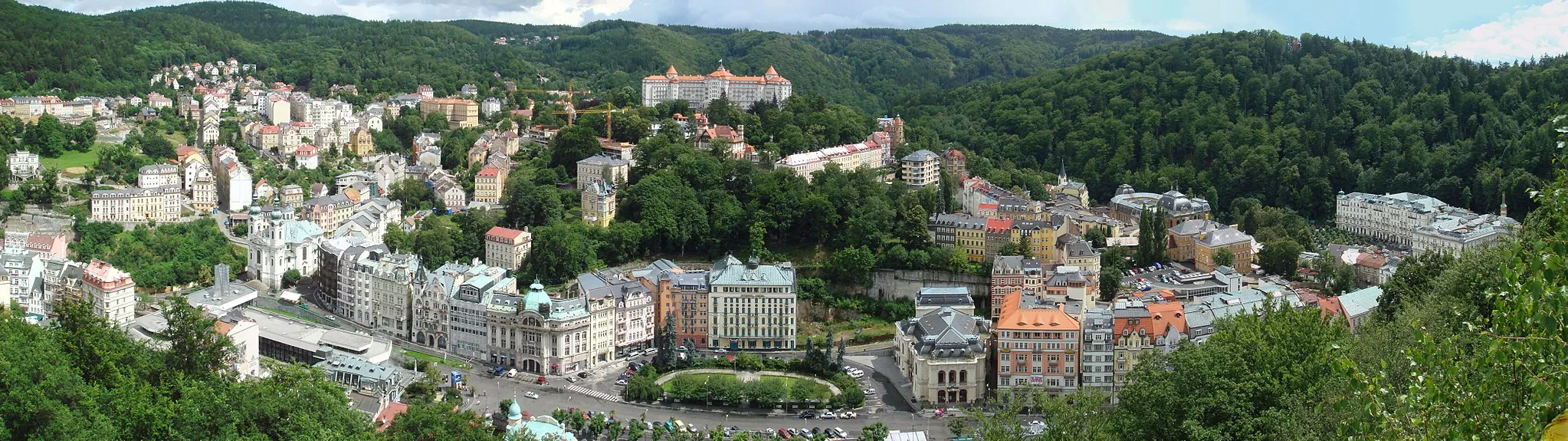 Photo showing: Panoramic photo of Karlovy Vary, Czech Republic.  Major sites in photo, from left to right: The dark grey, Soviet era Thermal Spring Colonnade (also called Hot Spring Colonnade or Sprudel) features a glass chimney.  Directly above it sits the twin-steeple Church of St. Mary Magdalene.  The large, stately building on the center hill is the Hotel Imperial.  Below it, to the right of the square, is the Opera House.  The Grandhotel Pupp is the large white building to the far right.  This was stitched together from five photos taken in quick succession.