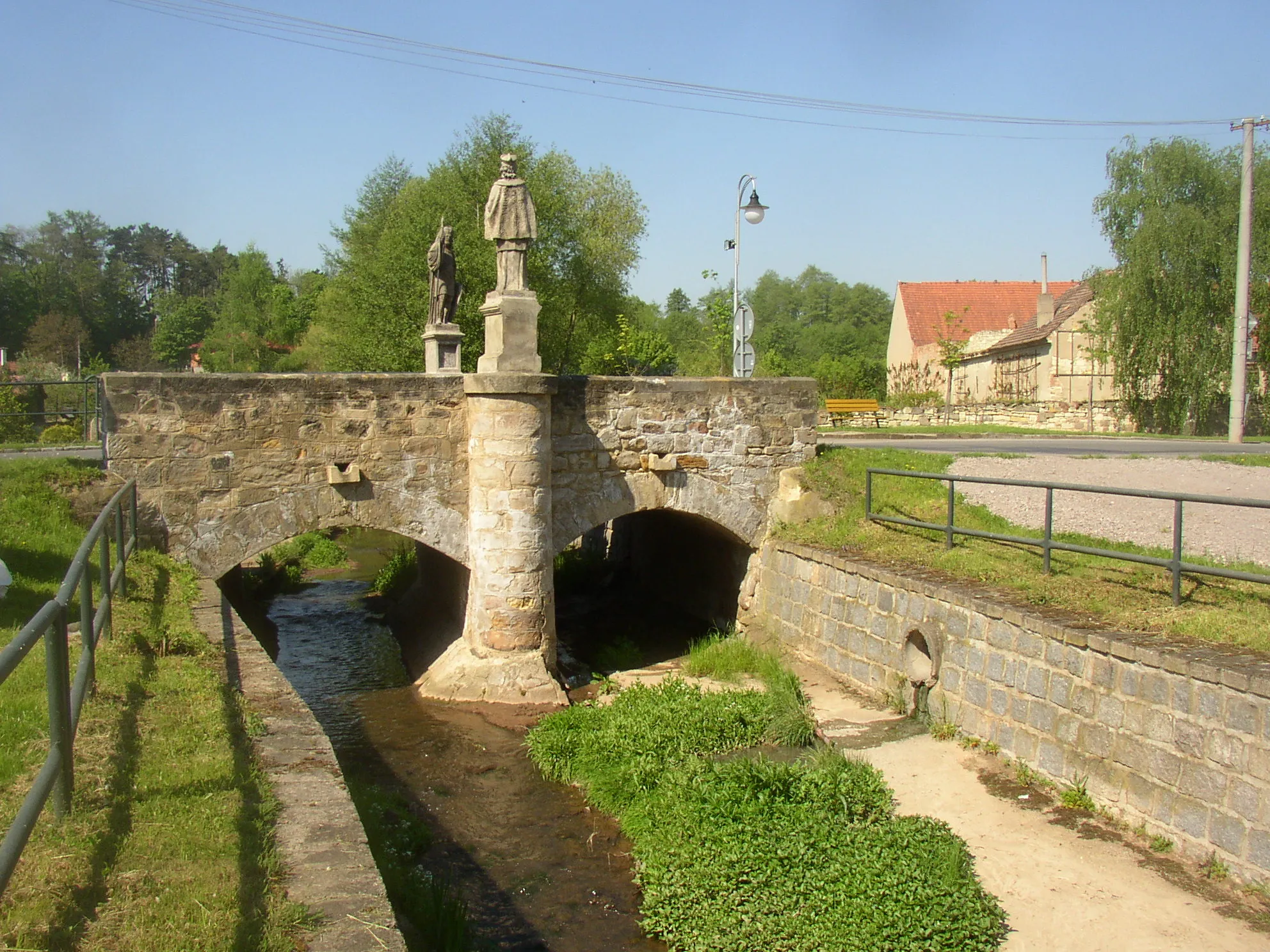 Photo showing: Stone arch bridge over the Bakovský potok stream in Královice village, Kladno District, Czech Republic. The bridge is decorated with pair of statues depicting St Wenceslas and St John Nepomucene.