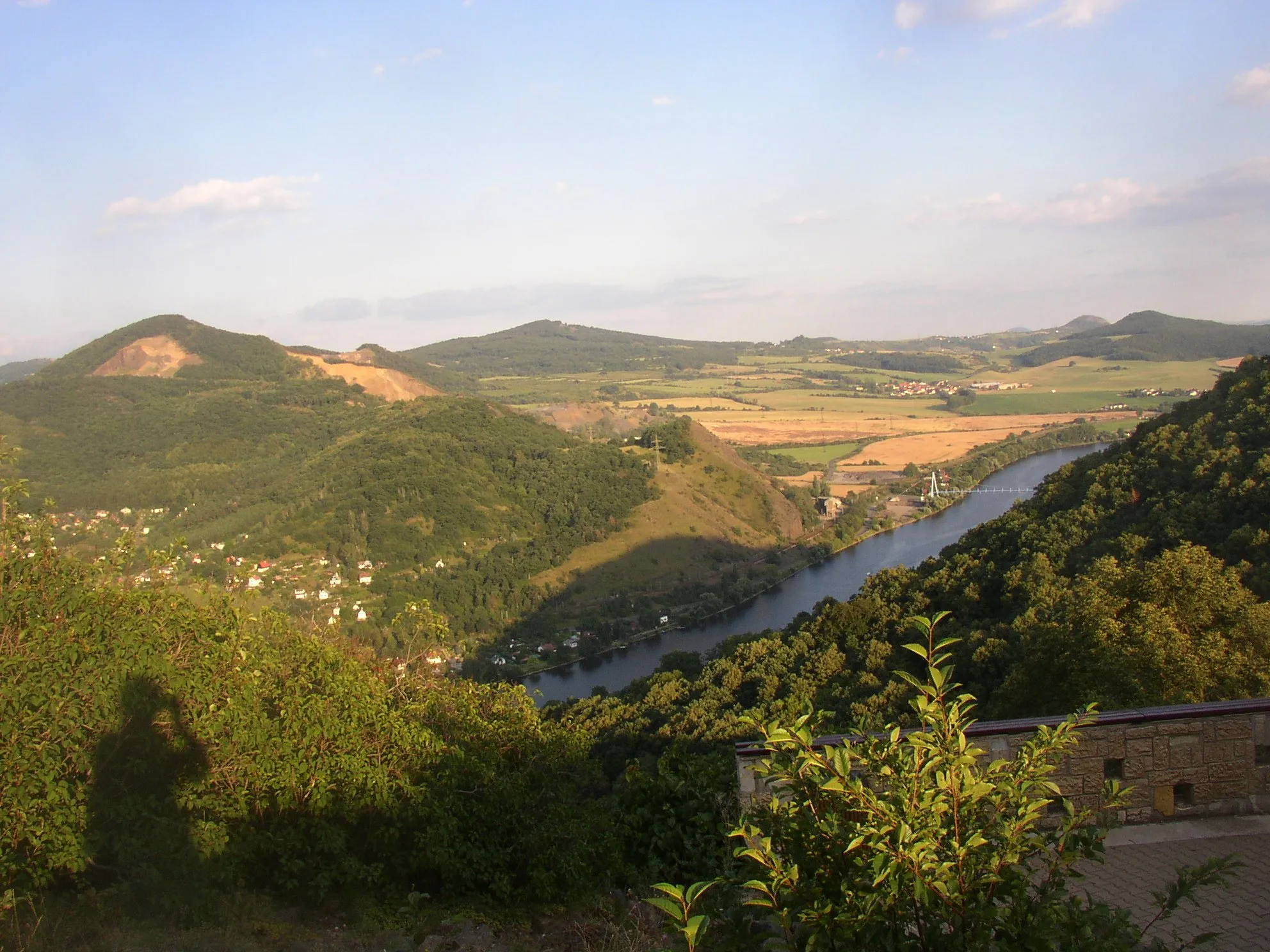Photo showing: České středohoří, Czech Republic. A view from lookout point next to St Barnara church in Dubice over the Elbe towards southeast. Deblík (459 m, left froreground), Plešivec (509 m, left background), Radobýl (399 m, right background behind Strážiště), Strážiště (362 m, right background). The village in the middle at foot of the hills is Řepnice, a part of Libochovany municipality