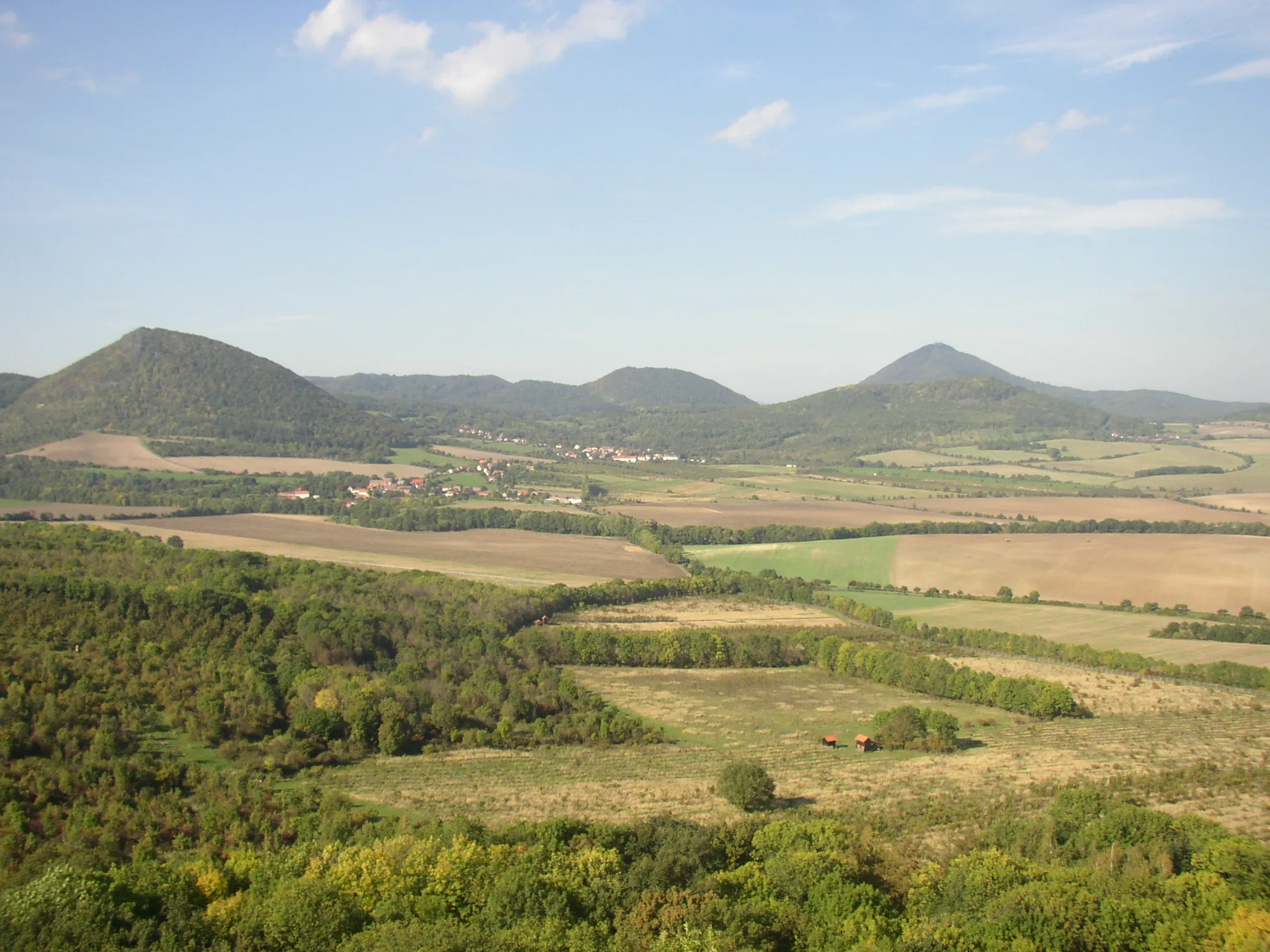 Photo showing: View from summit of Plešivec (477 m) in České středohoří Mts. towards north. In the left hill of Lipská hora (688 m), centre Milešovský Kloc (674  m), right Milešovka (837 m) with lower Medvědický vrch (571 m) at its foreground. Several small settlements belonging to Třebenice municipality are visible, the nearest in the left being Mrsklesy with Lipá and Medvědice beyond. In the right, at foot of Medvědický vrch, village of Kocourov.