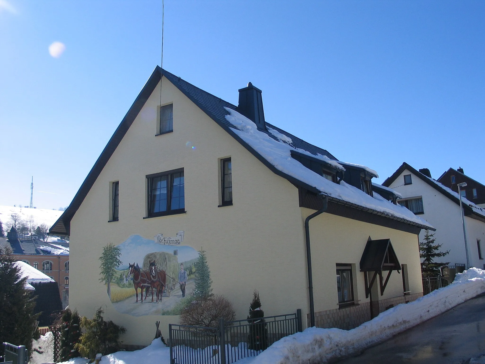 Photo showing: Ehemaliges Bauernhaus mit Fassadenbild (gemalt von Jürgen Schubert). Im Hintergrund unten die Geschwister-Scholl-Schule (Hauptstraße 70), oben der schneebedeckte Berg Knock (725,5 Meter) mit einer in den 1990er Jahren aufgestellten Sendeanlage.
