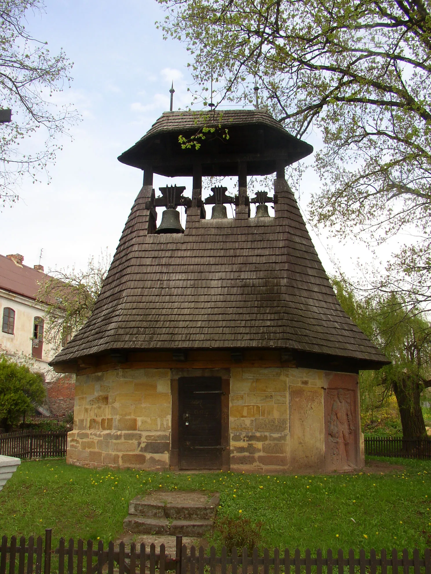 Photo showing: Neprobylice, Kladno District, Czech Republic. Belfry in centre of the village. This exact replica of an older belfry from about 16th century was constructed in 1896. The bells are original, from 15th and 16th century. Two Renaissance tombstones belonging to members of Pětipeský of Chyše and Egerberk family, who once owned the village, can be seen in wall at foot of the belfry.