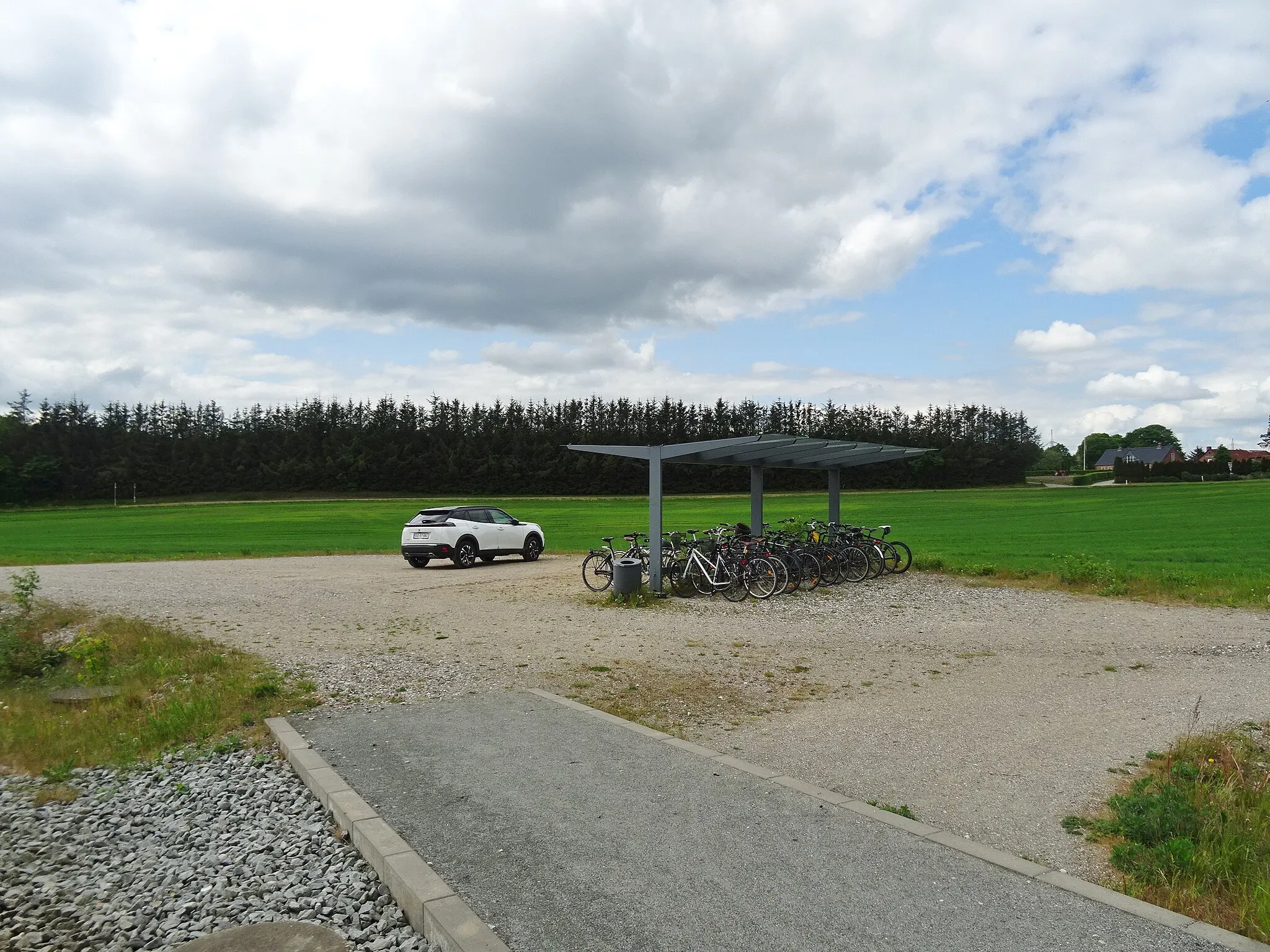 Photo showing: Parking lot and bicycle racks at Nye Station of Aarhus Letbane northeast of Aarhus in Denmark. There are only a few farms next to the station but it seems that quite a few people come on bicycles from the small city Elev a kilometer north of the station.