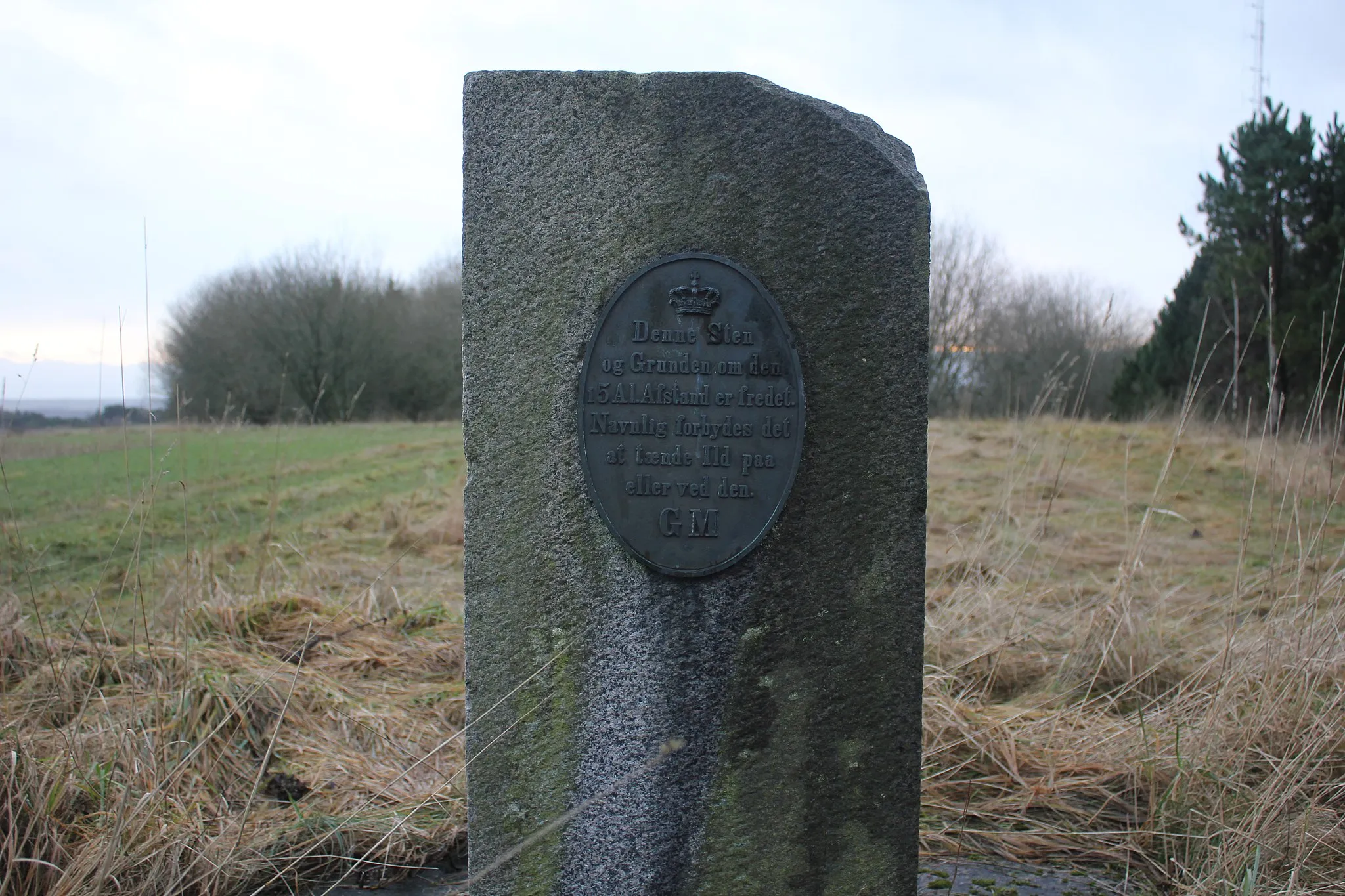 Photo showing: Reference point marker in Denmark. The plate on the stone states that "This stone and the area surrounding it for a distance of 3m is protected. Specifically it is forbidden to light a fire on or near [the stone]. [Signed] GM". The length is written on the stone as "5 Al", which is 5 Danish Ells (alen), roughly the equivalent of 3 meters. "GM" is the signature for the organisation "Graadmaalingen", which was the name of the Danish Geodata Agency between 1816 and 1842.