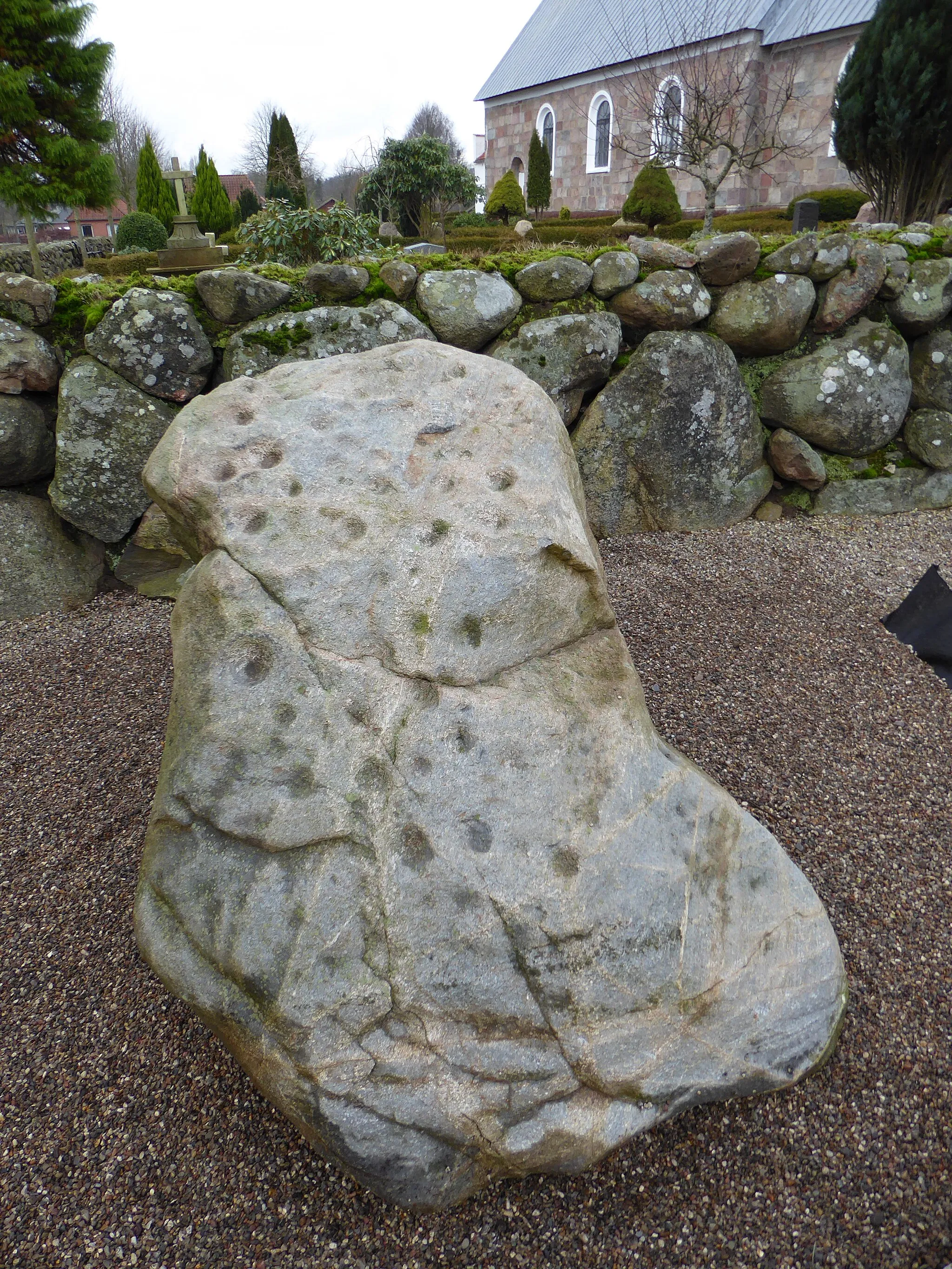 Photo showing: Skålstenen blev fundet i 1937 nær Vråvej 2 ved Øster Lindet. De mange fordybninger er formentlig udhugget i bronzealderen og har sandsynligvis været brugt i religiøs forbindelse. Den er nu opstillet ved kirkegården.