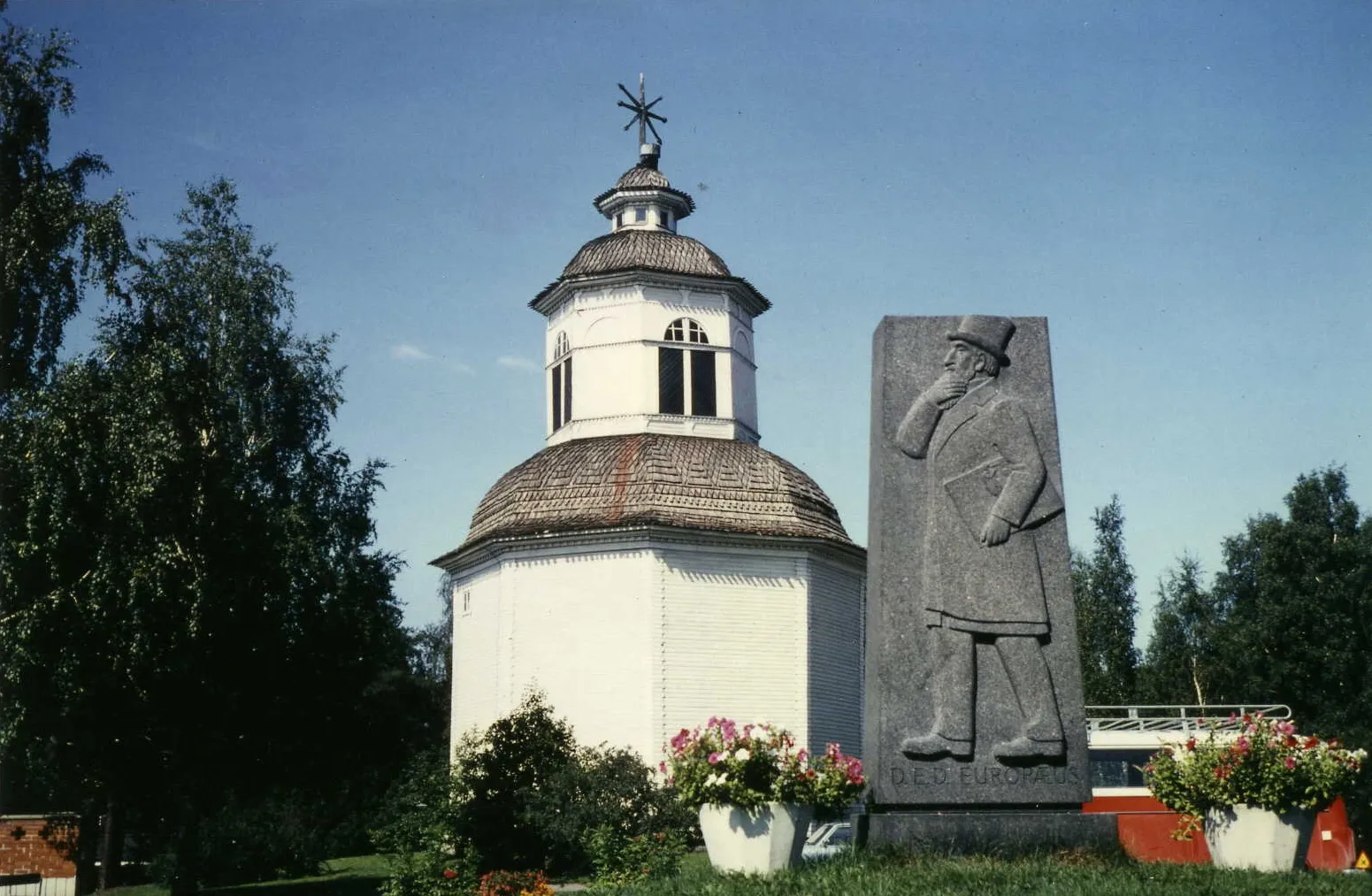 Photo showing: A belfry in Savitaipale, Finland and the memorial of D. E. D. Europaeus.