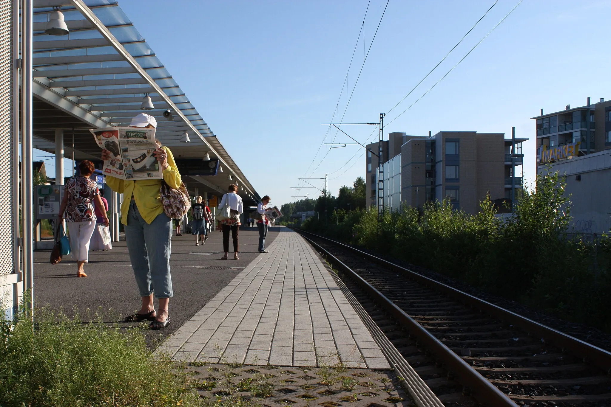 Photo showing: People reading newspapers while waiting for the train at Korso Railway Station in Vantaa, Finland
