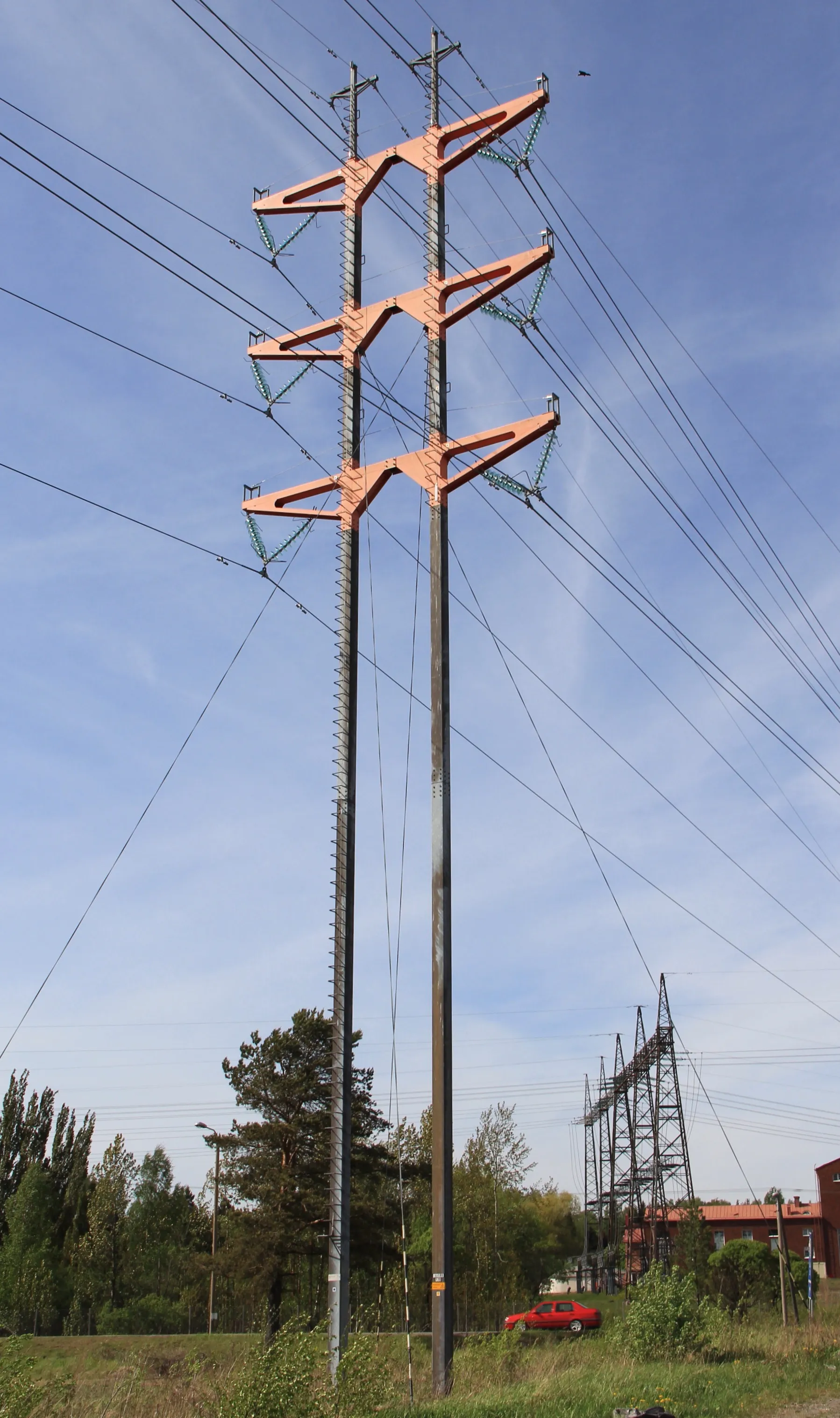 Photo showing: Guyed T-type 2-legged pylon of overhead power line in Virkkala, Lohja, Finland. - It carries two 110 kV lines. Pylon is designed by Studio Nurmesniemi interior designers and completed in 1996. Crossarms are painted vermillion. -Seen from southeast.