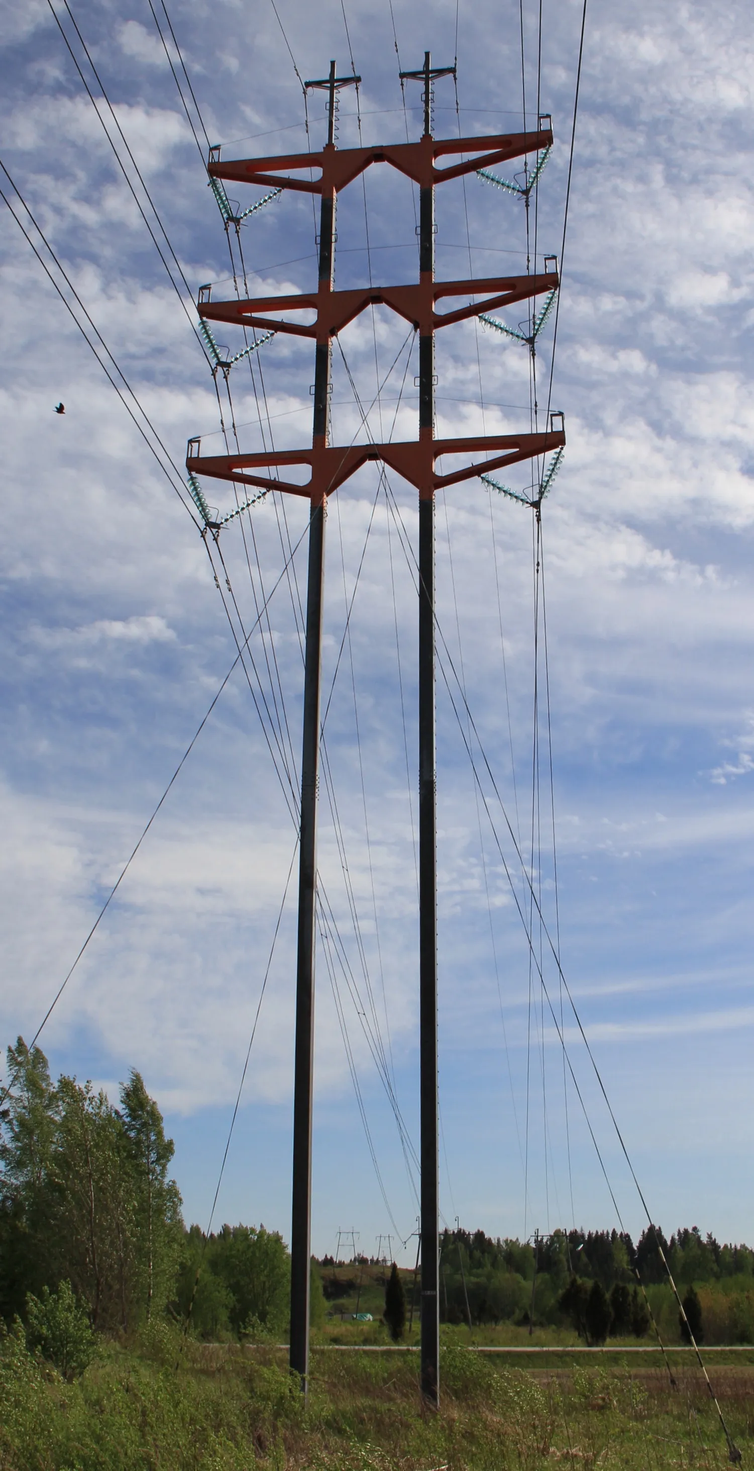 Photo showing: Guyed T-type 2-legged pylon of overhead power line in Virkkala, Lohja, Finland. - It carries two 110 kV lines. Pylon is designed by Studio Nurmesniemi interior designers and completed in 1996. Crossarms are painted vermillion. -Seen from northeast.