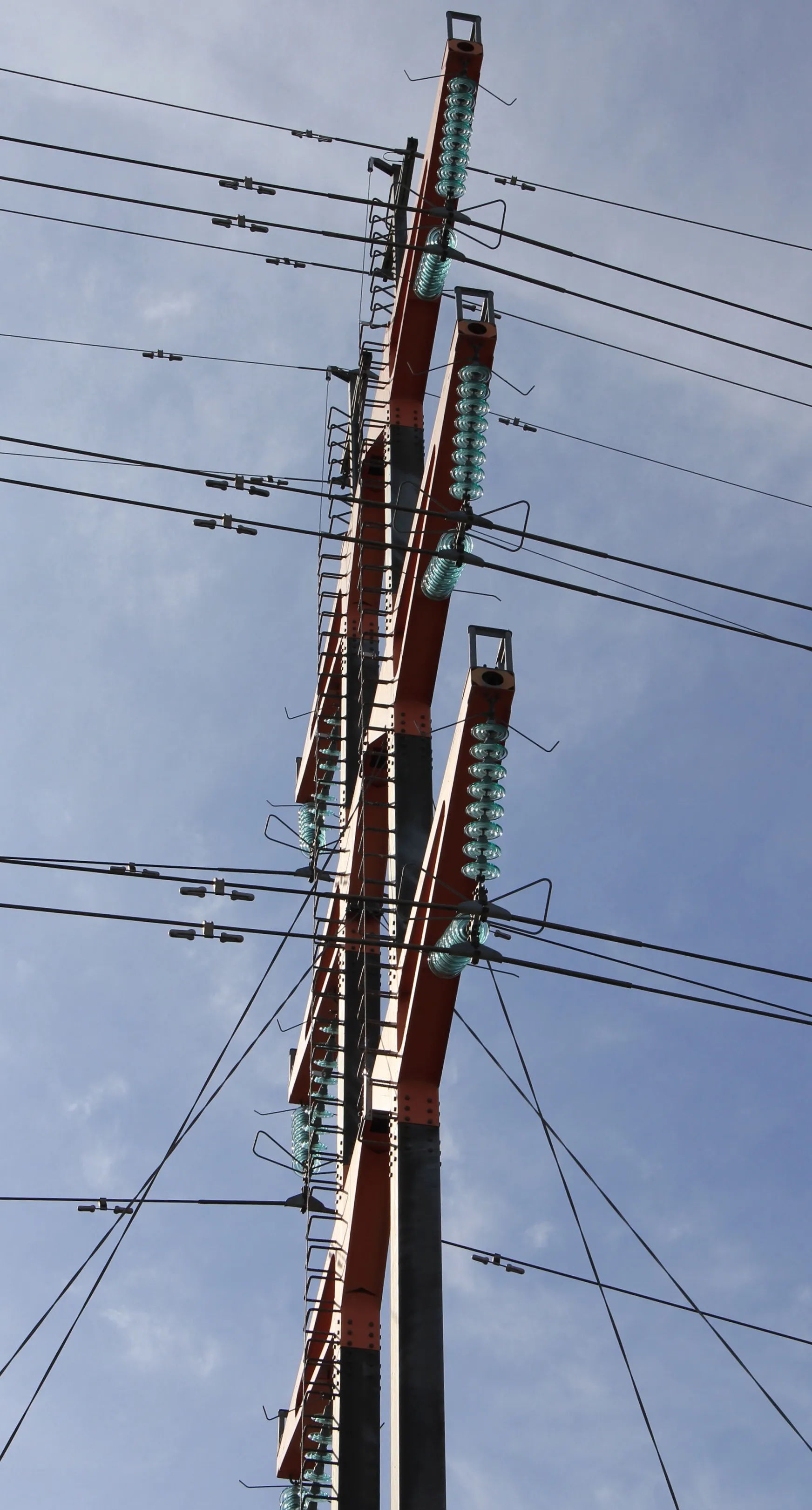 Photo showing: Guyed T-type 2-legged pylon of overhead power line in Virkkala, Lohja, Finland. - It carries two 110 kV lines. Pylon is designed by Studio Nurmesniemi interior designers and completed in 1996. Crossarms are painted vermillion. -Seen from northeast.