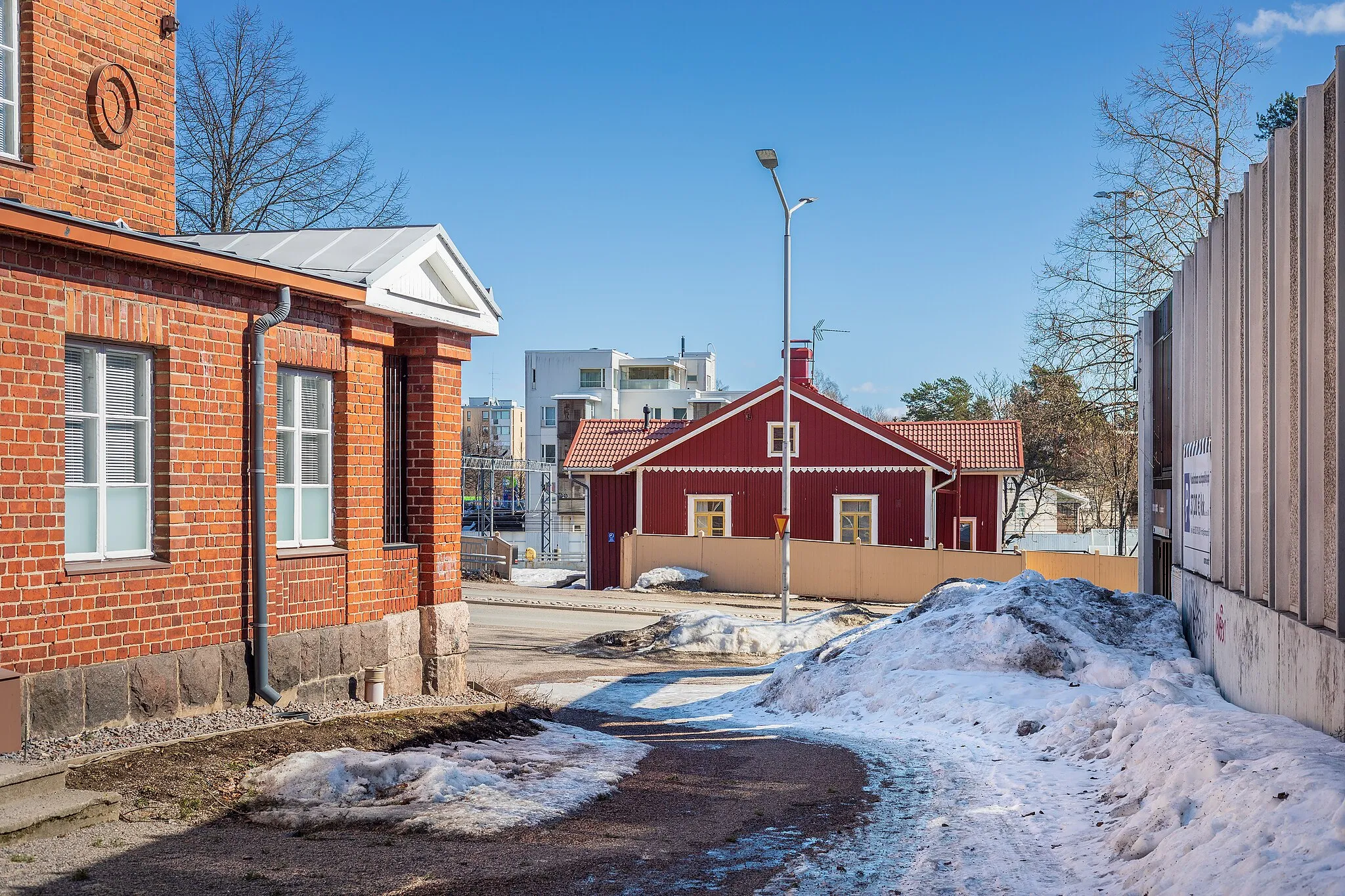 Photo showing: The wooden building of Asemantie 3, known as "Santarmien talo", as seen from a pedestrian path to the west in Kerava, Finland in 2022 April. The red tile building on the left is Sivistysvirasto (recently Kiinteistö Oy Nikkarinkruunu). Sivistysvirasto is estimated to be from 1923. Asematie 3 is estimated having been built in 1897.