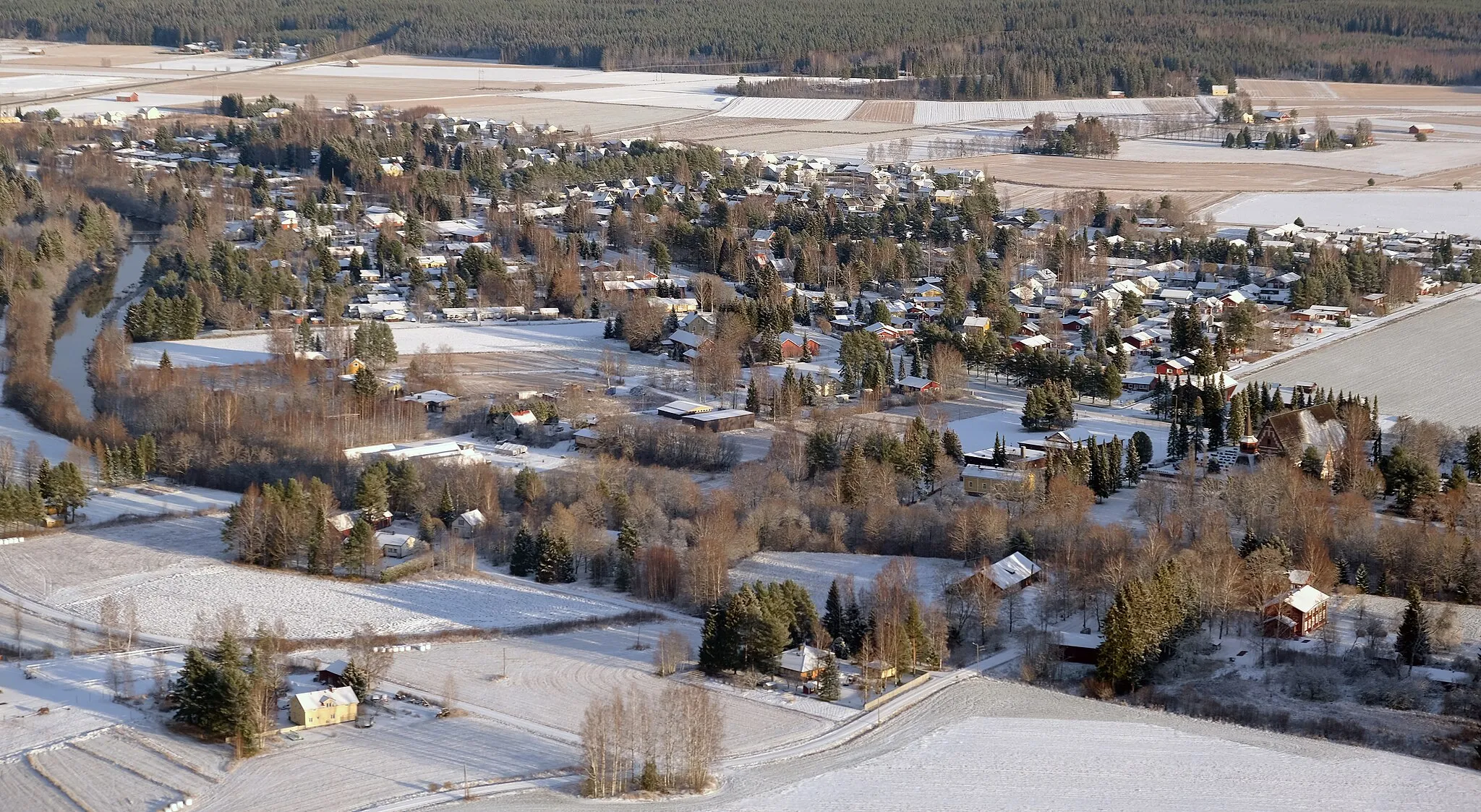 Photo showing: Aerial view of the Ulvilan kirkonseutu ('Ulvila's church area') looking northeast from above Saarenluoto. The Kirkkojuopa flows from left-top to right-bottom and the Saarentien silta ('Saari-road bridge') is near the meeting point of centre-middle and right-bottom. Ulvila Church and its cemetery can be seen at right-middle. Mynsteri residential area is in the middle-ground. Valtatie 11 ('Highway 11') cuts across left-top in the distance. Note: Image placements assume overlay of grid comprising three columns (left, centre, right) and three rows (top, middle, bottom) to create nine cells of identical dimension.