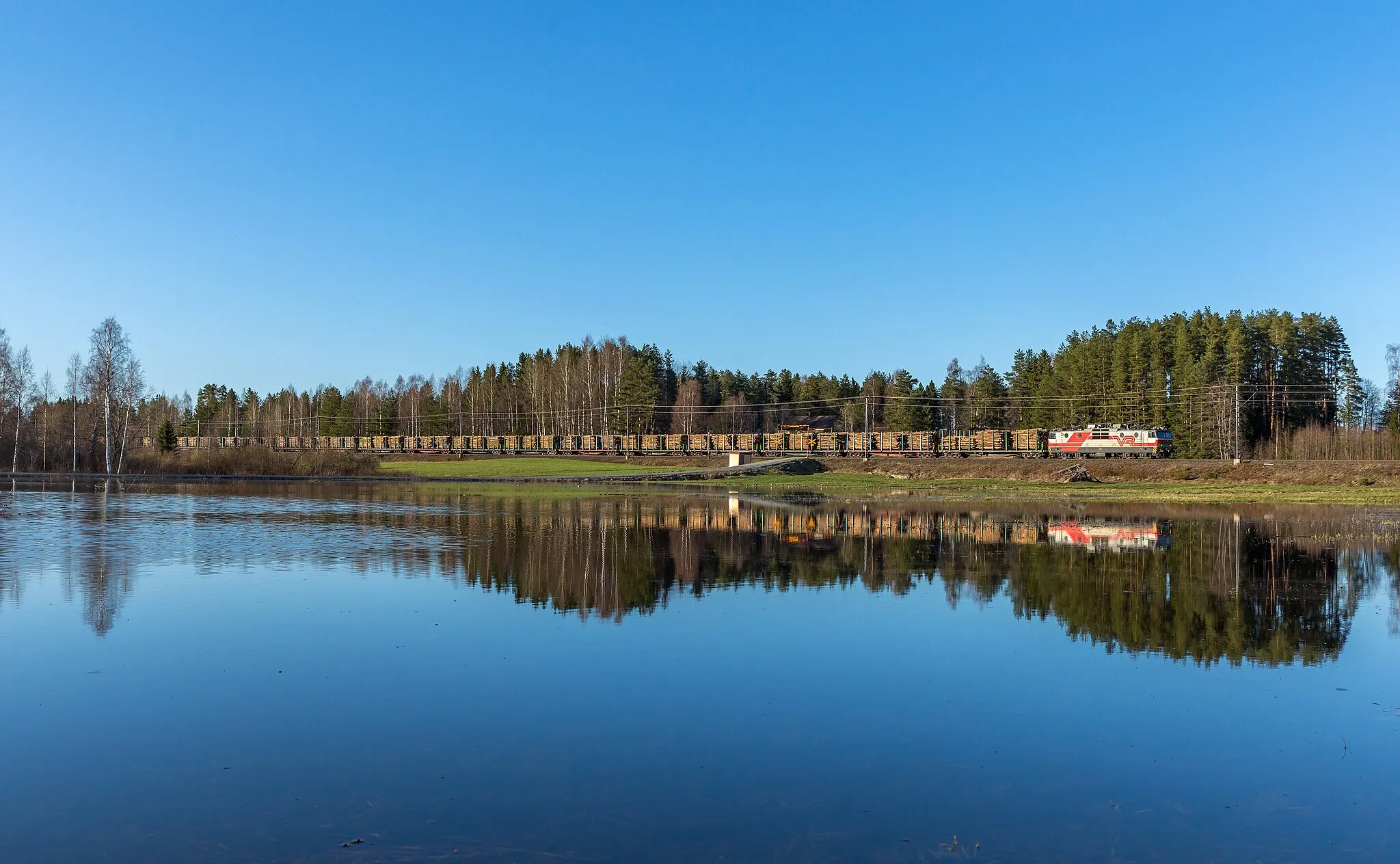 Photo showing: VR-Yhtymä Oy's Sr1 3041 with a lumber train between Lapinlahti and Siilinjärvi, Finland. The lake in the foreground is actually a field flooded due to high lake water levels.