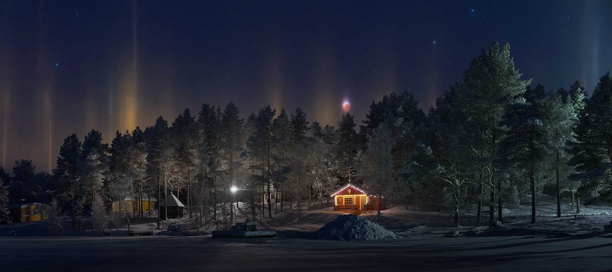 Photo showing: A lunar eclipse and light pillars as seen from lake Särkijärvi in Muonio, Lapland, Finland in 2019 January. The light pillars are an atmospheric optical phenomenon caused by light interacting with ice crystals in the air in freezing temperatures.