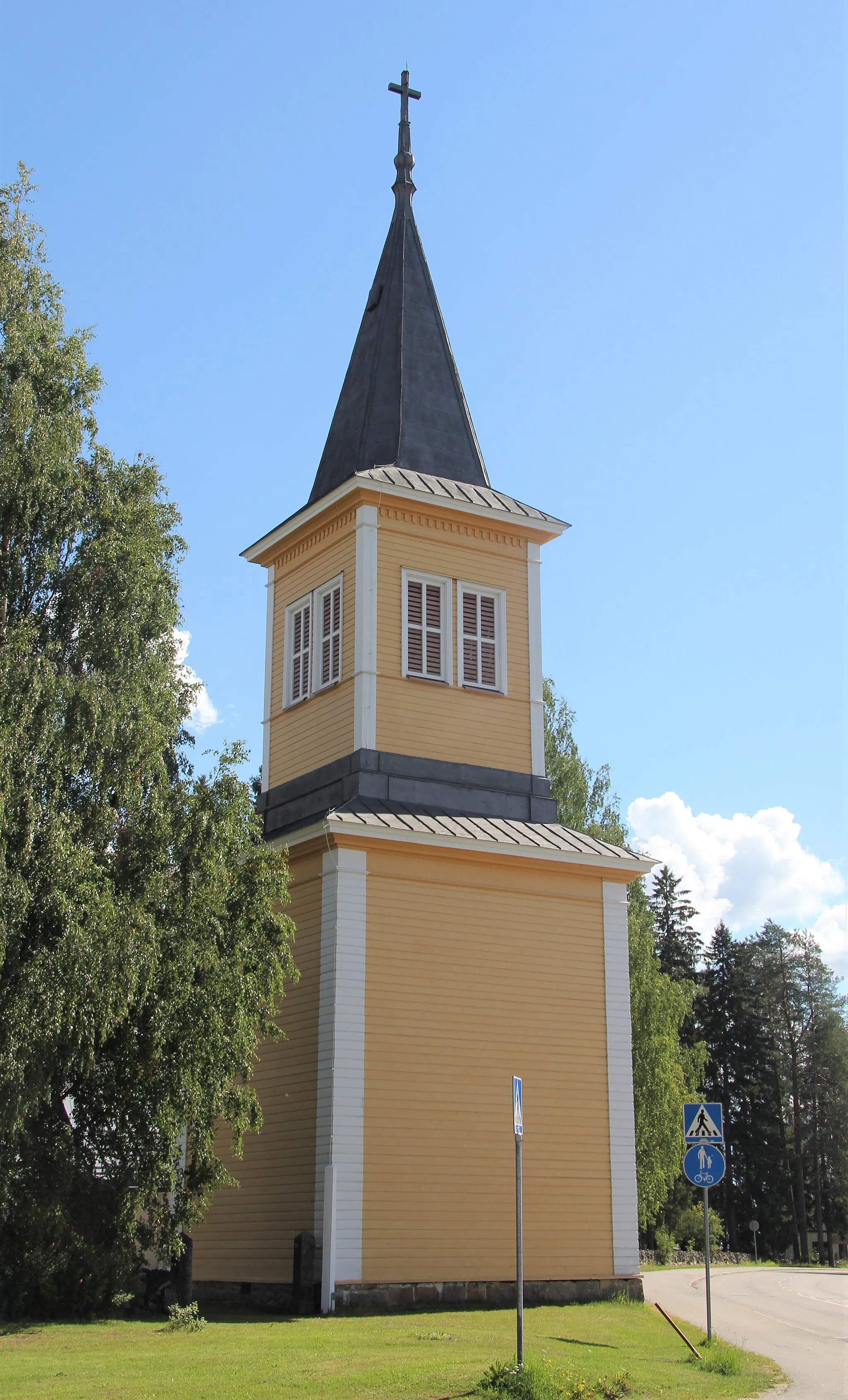 Photo showing: Rautavaaran kaksinivelinen kellotapuli vuodelta 1888 (arkkitehti Lohrmannin v. 1858 allekirjoittamien piirustusten  mukaan). Kellotapuli liittyi C. Bassin piirrustusten mukaan 1825-1827 rakennettuun ensimmäiseen kirkkoon, joka lopullisesti valmistui vasta 1864. Tuo kirkko paloi vuonna 1979. Sakari Aartelon ja Esa Piirosen suunnittelema uusi kirkko valmistui 1982. Tapuli on säilynyt  tornin kelloluukkujen muuttamista lukuun ottamatta 1900-luvun vaihteen asussa. Rautavaaran kellotapuli ja kirkko sijaitsee Rautavaaran kirkonkylässä osoitteessa Savontie 13 (Savontien ja Kirkkotien kulmaus), Rautavaara. Koordinaatit kellotapuliin.