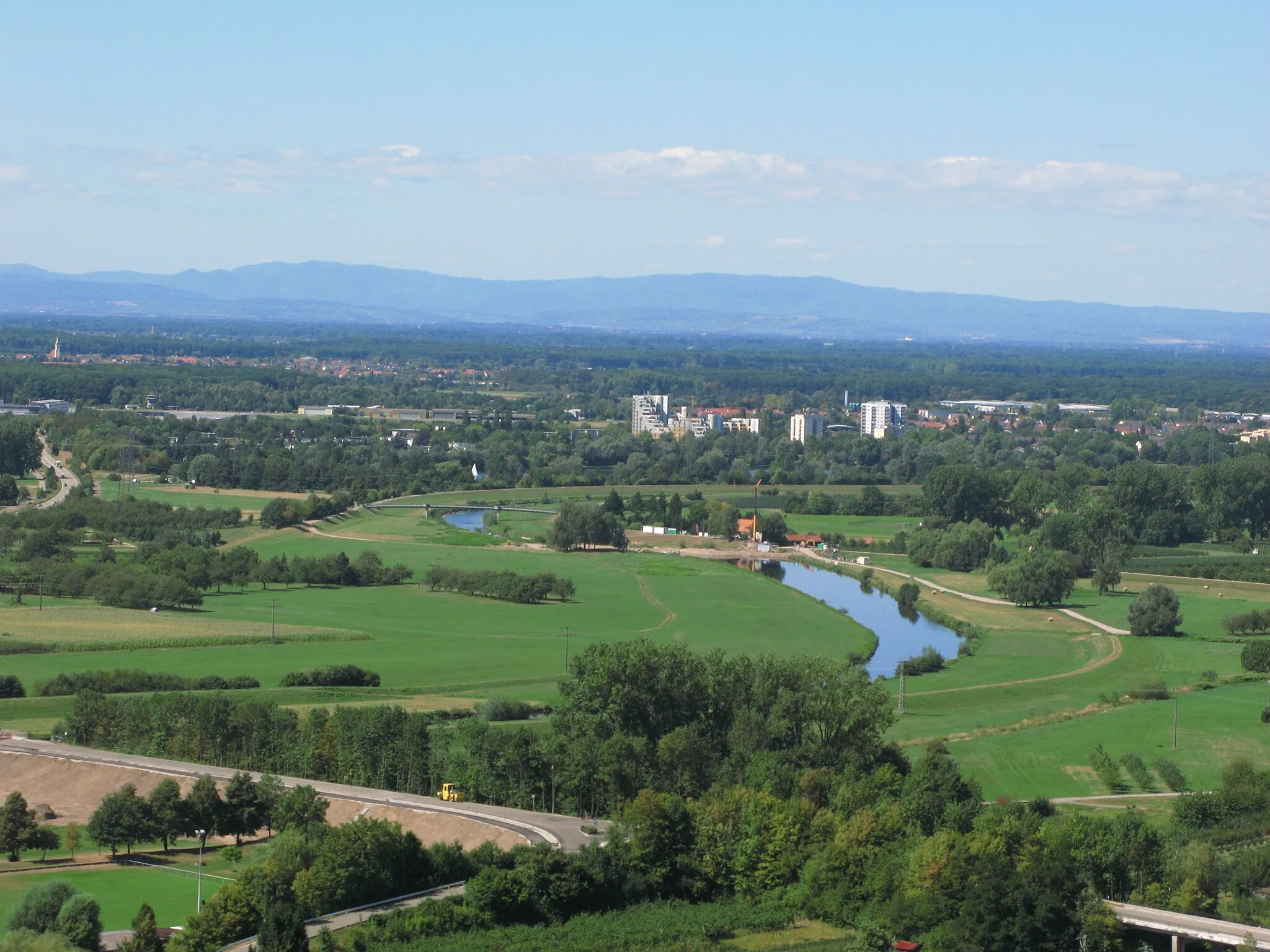 Photo showing: Blick vom Ortenberger Schloß auf die Kinzig und den Großen Deich, an dem zu dieser Zeit ein Wasserkraftwerk installiert wurde, an einem Spätsommertag mit sehr guter Sicht. Dahinter erkennt man rechts die Wohnbebauung des Stadtteils Uffhofen, auf etwa gleicher Höhe links die Hallen des Flugplatzes, hinter denen Schutterwald auszumachen ist. Den Hintergrund bilden die Vogesen mit dem Donon. Von der Bildmitte nach links kann man den Höhenzug ausmachen, der das Tal der Breusch von der Oberrheinebene abgrenzt.