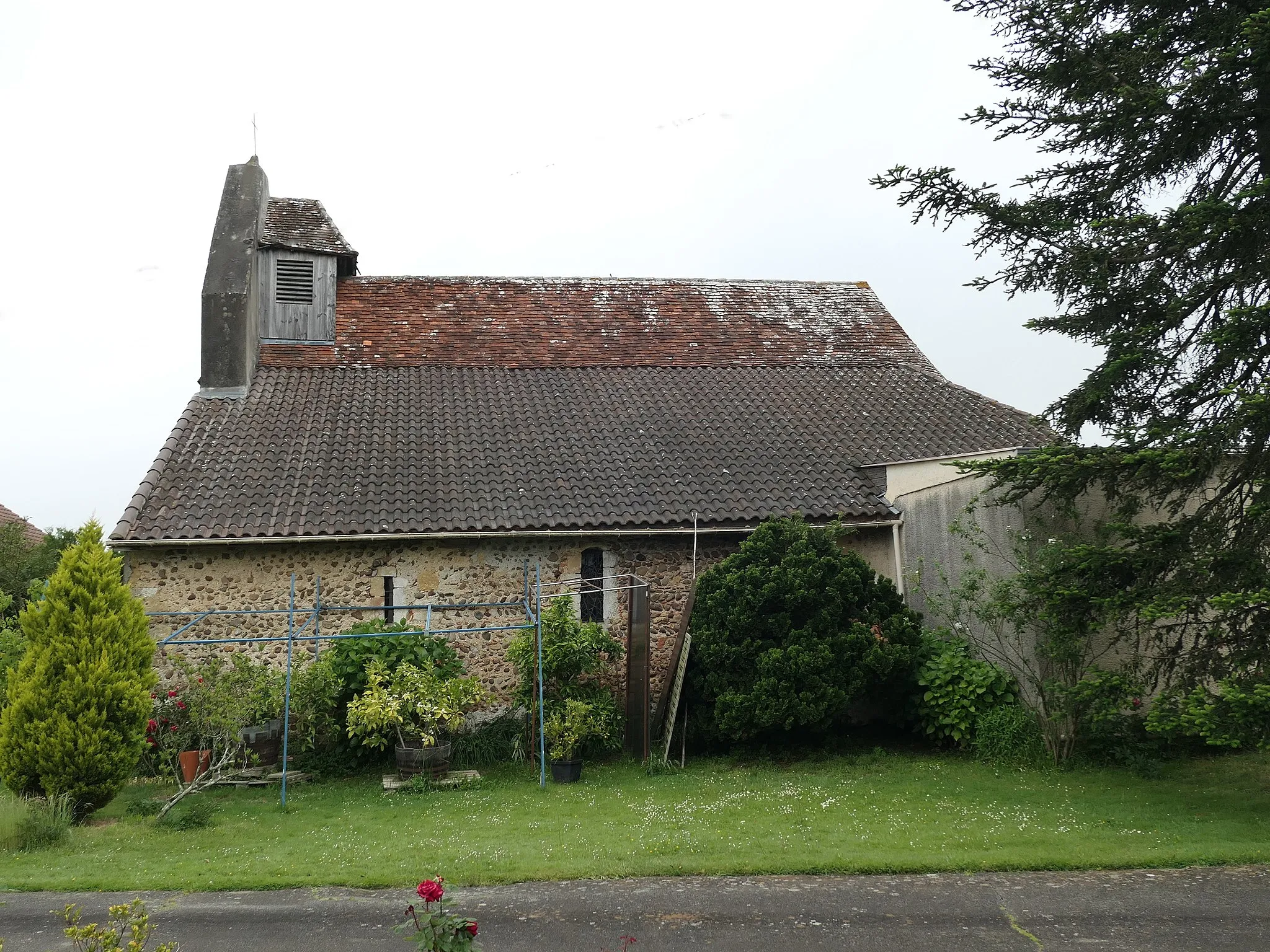 Photo showing: vue de côté, toiture en tuiles, clocher mur en façade avec un petit pavillon abritant la cloche