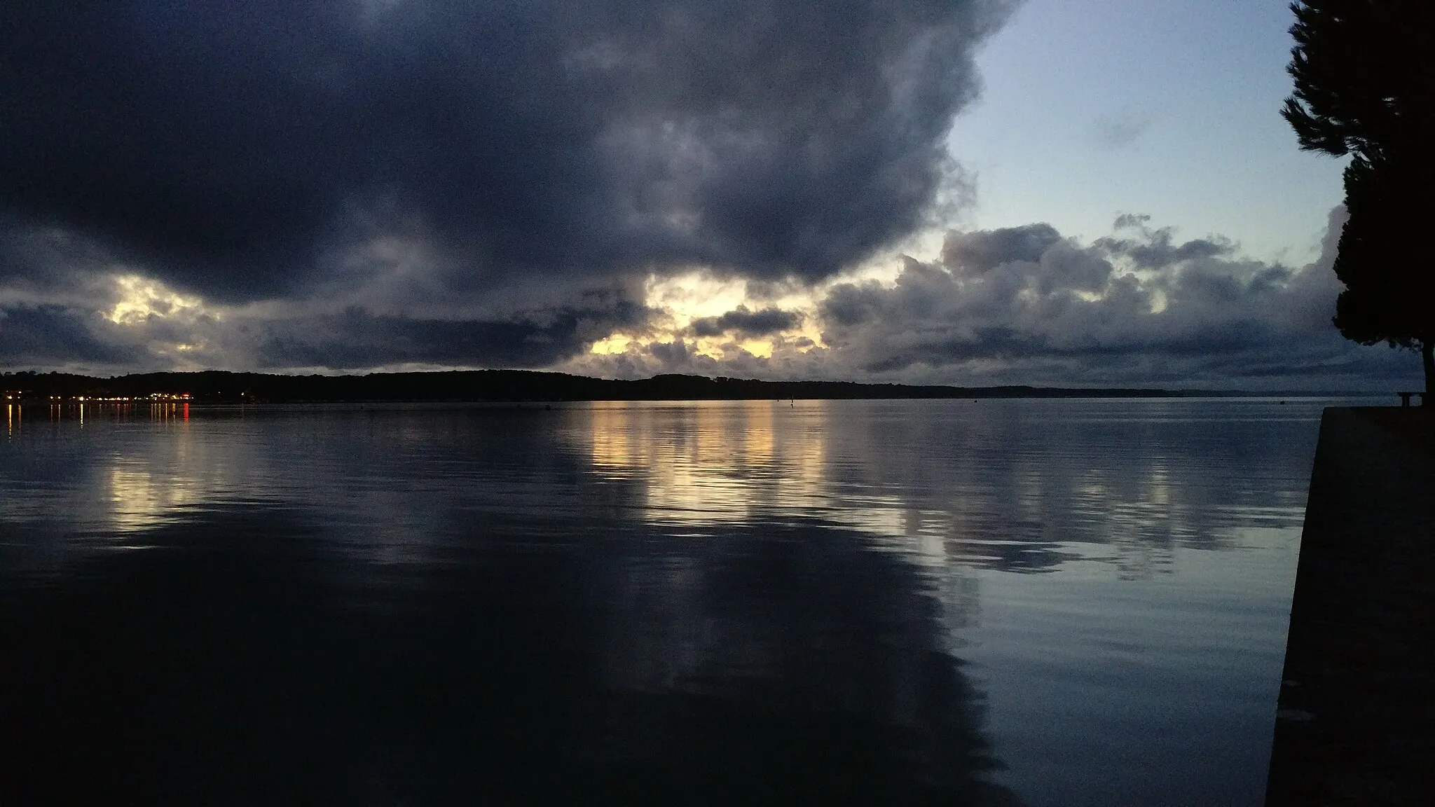 Photo showing: Une simple vue de l'étang de Carcans (Gironde, France) au crépuscule. Reflet du soleil mourrant et des éclairages sur l'eau. Il y a un traitement de la part de l'application de prse de photos.