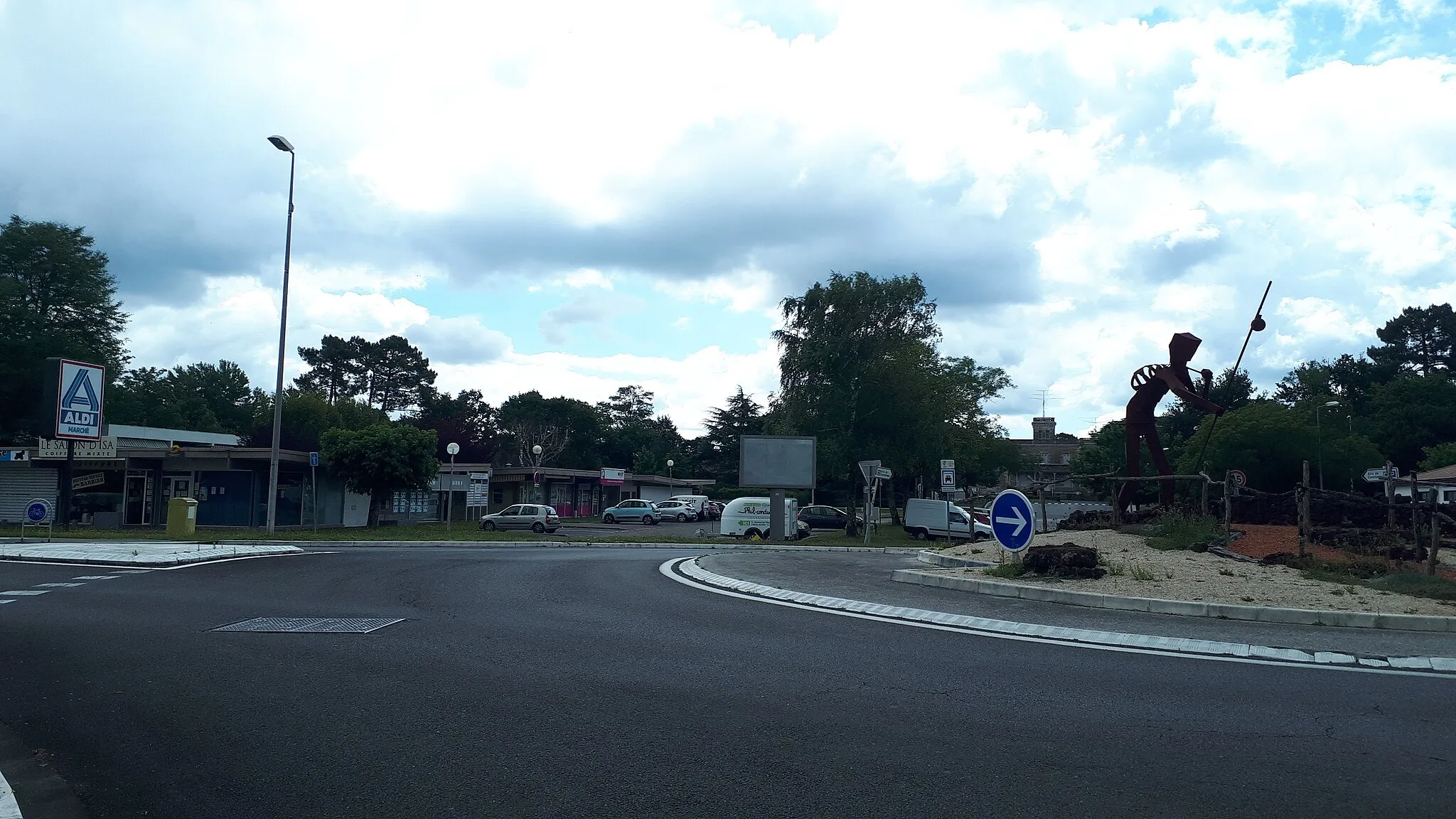 Photo showing: Rond point de Réjouit avec la sculpture du pèlerin de St Jacques de Compostelle en fer. Au fond, le château de Choisy, servant à l'école de musique. Au second plan, le centre commercial de Cestas Réjouit avec l'Agence Postale Communale.