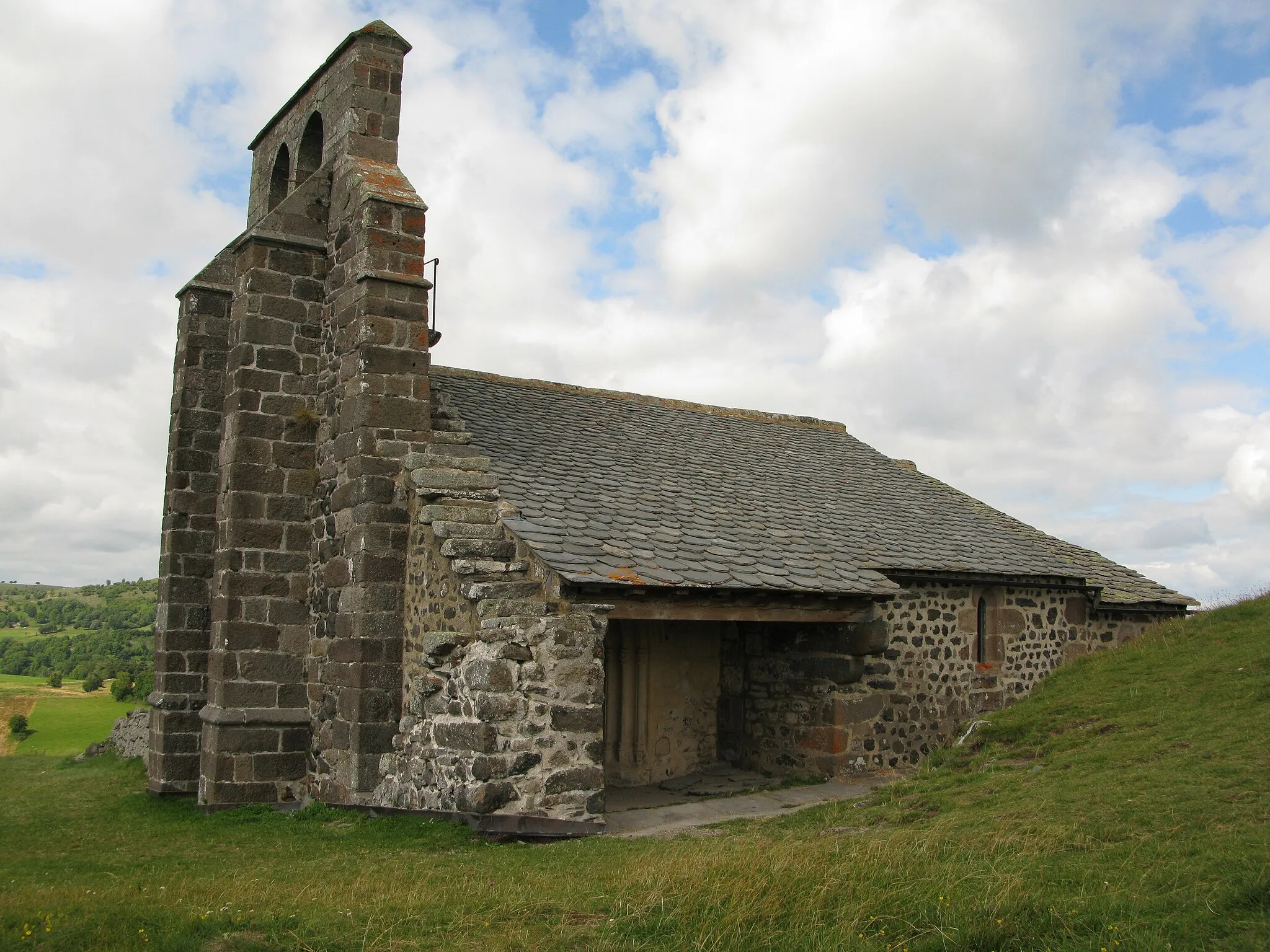 Photo showing: Vue de trois-quart sur la chapelle Saint-Antoine depuis le sud. Sur la gauche, le clocher à peigne. Au centre, la porte d'entrée. La toiture principale est couverte d'ardoises. La toiture du choeur est couverte de lauzes. Sur la droite du clocher, un escalier extérieur en pierre permet d'accéder au clocher.