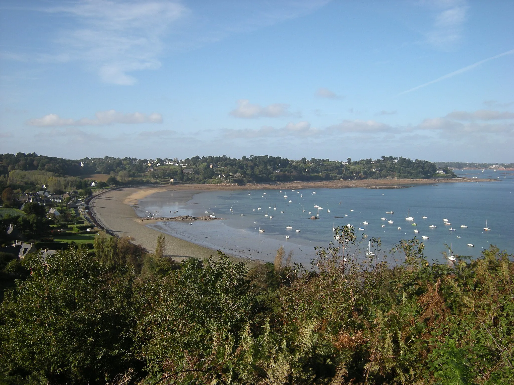 Photo showing: Ploubazlanec, Côtes-d'Armor, Bretagne, France. Vue vers le nord de l'anse de Launay, depuis la Croix des Veuves sur la pointe de la Trinité au nord de Pors-Even. En bord de plage, le village de Launay. L'anse est fermée au nord-nord-ouest par la Pointe de l'Arcouest, avec en face de nous le flanc sud-est de cette pointe (la façade nord-ouest de l'anse). Sur cette façade nord-ouest de l'anse, côté gauche, presque sur la plage : la petite maison aux murs roses est la maison du parc ; à sa droite, toujours près de la plage : 'Roc'h Ar Had', la maison construite en 1904 par Louis Lapicque; à la droite de celle-ci, assez près de la plage : la maison de Marie Curie ; tout à fait à la pointe : la maison des Betttencourt. L'île Saint-Riom n'est pas visible, elle se trouve derrière nous légèrement sur la droite.