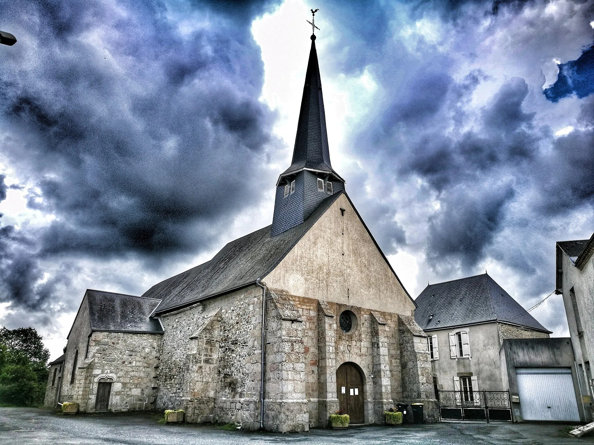 Photo showing: Vue de l'église catholique de la commune de Lourdoueix-Saint-Pierre, Creuse, France, depuis la Place de l'Église. L'effet lumineux des nuages à été accentué pour mieux détacher le bâtiment de l'arrière-plan.