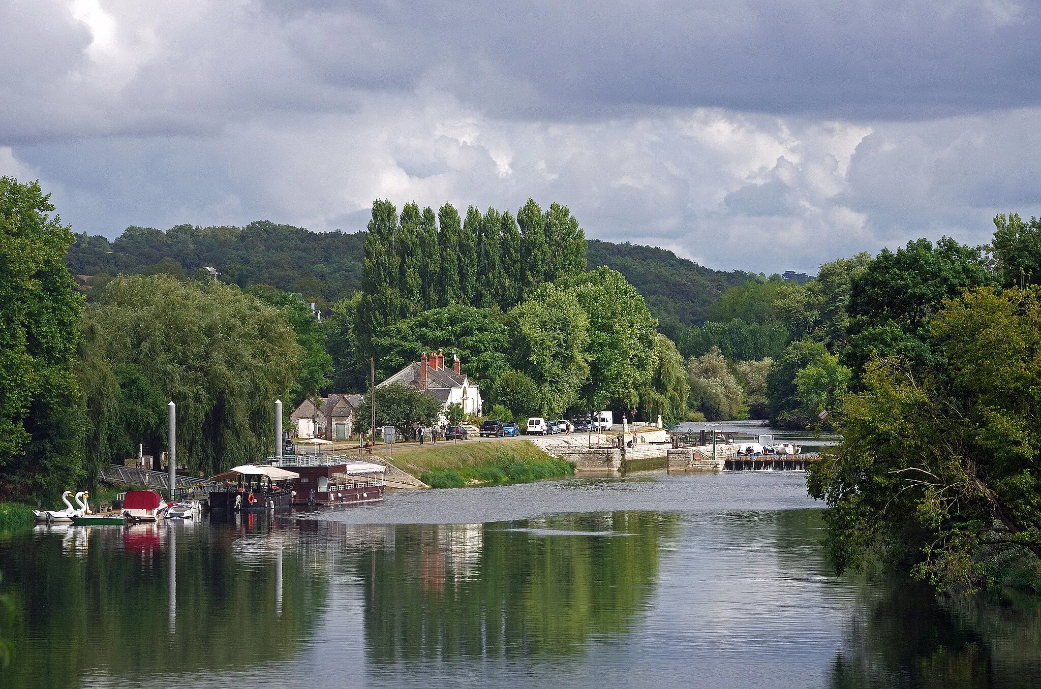 Photo showing: Chisseaux (Indre-et-Loire)
Le Port Olivier et l'écluse.
Au XIXe siècle, le Cher est canalisé depuis Noyers-sur-Cher jusqu'à Saint-Avertin.
La commune, est pourvue en 1830-1840 d’un barrage à aiguilles sur le Cher, d'une écluse rive droite.
L'écluse mesure 35 m de long sur 5,15 m de large. Le barrage est composés d'aiguilles en bois de 2,50 m de haut sur 7 cm de large et d'un déversoir sur la gauche.  Le 7 juin 2010 le déversoir de Chisseaux tue 2 navigateurs qui tentaient de franchir le barrage. Le dangereux phénomène de rappel* est trop souvent méconnu.

Le rappel est une : "Perturbation dangereuse dans l’écoulement de l’eau pouvant survenir en bas d’une chute d’eau. Cette perturbation entraîne une émulsion de l’eau, un mouvement de surface qui ramène l’eau vers la chute, un affouillement qui creuse une excavation au pied de la chute. Les barrages artificiels ou des chutes naturelles peuvent avoir un rappel  à leur pied ce qui interdit totalement leur franchissement." (rivieres.info/lex/lexique.htm) (rivieres.info/secu/84-barrages.htm)