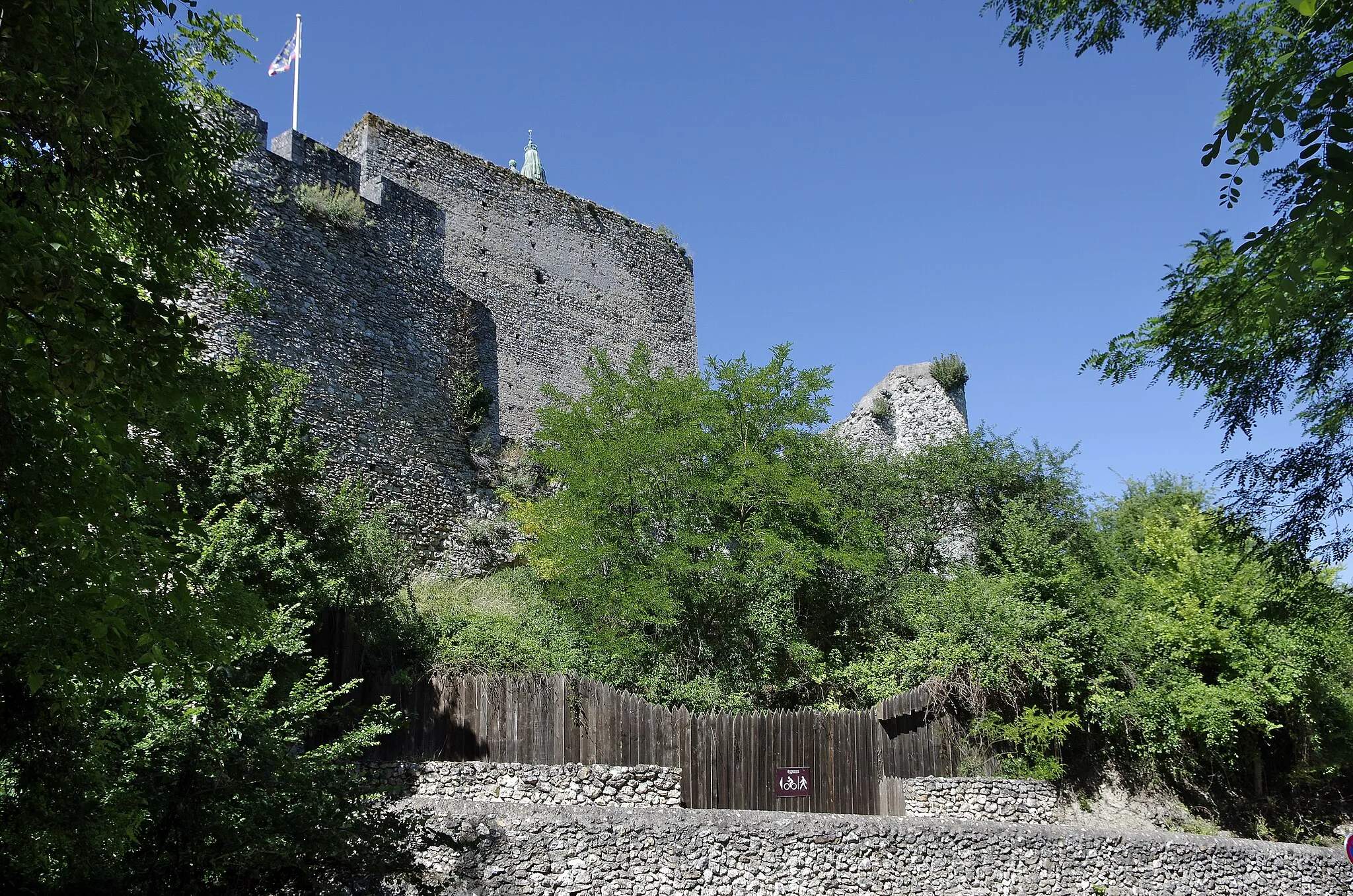 Photo showing: Montbazon (Indre-et-Loire)
La forteresse de Montbazon.
C'est un des plus ancien édifices médiévaux de France et l'un des premiers donjons féodaux.
Foulques III Nerra (le Faucon Noir)* fit édifier sur cet éperon rocheux qui domine la vallée de l'Indre, une motte castrale avec un donjon en bois qu'il remplaça plus tard par un donjon en pierre. Foulques Nerra construira sa forteresse sur les terres des moines de la puissante abbaye de Cormery qui s'en plaindront au roi de France Hugues Capet.
Foulques Nerra fut un grand bâtisseur de forteresses et de donjons  aux frontières de son domaine. Il construira ou améliorera une vingtaine de sites fortifiés.
Le donjon mesurait 36 m de hauteur à l'origine (une dizaine de mètres en moins aujourd'hui). Les murs ont une épaisseur d'environ 3 m à la base. Le donjon comprenait une cave et trois étages. Il était couvert par un toit à quatre pans. Les nobles restaient dans l'étage supérieur. On entrait, grâce à une échelle, dans le donjon, par une porte, sur la façade nord, située à 6 à 7 mètres du sol.
Le fils de Foulques Nerra, Geoffroy Martel, ajouta au donjon, vers 1050, un "petit donjon", accolé côté ouest. Ce "petit donjon" permettait l'accès au grand donjon par le premier étage.
Au XIIe siècle, Henri II Plantagenêt, roi d'Angleterre, descendant de Foulque, développera de manière importante la forteresse ( murailles, haute cour, chemin de ronde). Montbazon était entré dans ses domaines par son mariage avec Aliénor d'Aquitaine (qui était de la Maison de Poitiers).
Philippe Auguste prendra la forteresse en 1205, il en profitera pour faire construire de nouvelles tours et un second rempart.
La forteresse devient ensuite la propriété de différentes familles : Mirabeau, Savary, Craon, La Rochefoucault, Rohan*. Familles qui n'y résidèrent qu'occasionnellement.
Vers 1425 débutera la construction d'un nouveau château face au vieux donjon: le "Château-Neuf". Charles VII et Louis XI résideront régulièrement dans ce château.
Au XVIe siècle, Montbazon est le deuxième plus riche duché-paierie du royaume. Le deuxième château construit au XVe siècle, face au donjon, sera démoli au milieu du XVIIIe siècle pour la construction de nouvelles routes dont la plupart subsistent encore aujourd'hui. En particulier, une nouvelle route traverse tout Montbazon, c'est la route de l'Espagne (notre N 10). Un canal est aussi creusé dans la prairie, pour dévier un bras de l'Indre, et un nouveau pont est construit. Le Château Neuf servira alors de carrière, ainsi qu'une partie des remparts, pour construire la route.  Il ne reste qu'une seule porte : la porte des moulins. Le donjon survécut.
Le donjon reste occupé jusqu'en 1782. En 1791, le haut du donjon s'effondre ainsi que le "petit donjon". En 1797, un coup de foudre lézarde le donjon, dont la fissure est encore visible.
Le donjon servit un temps pour l'installation d'un sémaphore Chappe. Il ne fonctionnera que de 1823 à 1852. Le télégraphe Chappe permettait la transmission de signaux visuels par des bras articulés. Il ne fonctionnait évidemment que de jour et par temps clair. Le télégraphe Chappe sera vite remplacé par le télégraphe électrique. La balustrade en fer, à l'angle sud-ouest est le seul témoin restant de ce poste télégraphique.
C'est l'abbé Chauvin, curé de Montbazon de 1848 à 1890, qui eut l'idée d'utiliser le donjon comme support pour une statue de la vierge. L'idée fut finalement adoptée, et, la statue, de plus de 9 m de hauteur, installée à l'angle nord-est du donjon, le 4 novembre 1866. La statue est constituée de plaque de cuivre assemblées par rivetage, et l'intérieur remplit de pierres et de ciment. La statue fut largement subventionnée par l'impératrice Eugénie.
En 1922, un architecte états-unien, William Perry Dudley, achète le donjon et entreprend des travaux de consolidation.Il reconstruira la tour ouest et ajoutera  un logis dans le style Renaissance dans lequel s'installera son amie, l'artiste peintre Lilian Whitteker.
Le donjon est actuellement la propriété de monsieur Harry Atterton qui a ouvert le donjon au public depuis 2003. 
.
.
.

Foulques III Nerra (né vers 972, 1040). Comte d'Anjou de 987 à sa mort. Fils de Geoffroi Ier Grisegonelle et d'Adèle de Vermandois. Personnage hors du commun, Foulques Nerra régna sur l'Anjou pendant plus de cinquante ans.  Brutal mais pieux, il fit trois fois le pèlerinage de Jérusalem pour expier ses nombreux crimes.
Il sut défendre et agrandir son domaine, contre ses voisins les comtes de Blois et du Maine et les évêques du Mans. Son fief deviendra un fief direct de la couronne en 987. 
Il vainquit les Bretons à la bataille de Conquereuil en 992. Bataille dans laquelle il tua, de ses propres mains, le comte de Rennes Conan Ier.
Battu par le comte de Blois, par Eudes III, il fut sauvé par l'intervention du roi Robert Ier.  
En 1025, il prend Saumur à Odon de Champagne. Il  annexa les Mauges ainsi qu'une partie de la Touraine, et étendit sa suzeraineté sur le Vendômois et le Maine.
Il mourut au retour d'un pèlerinage en Terre Sainte, à Metz, le 21 juin 1040, à l'âge d'environ 70 ans.
En 989, il épousa Elisabeth, fille du comte Bouchard de Vendôme, un fidèle de Hugues Capet.
En seconde noces, il épousa Hildegarde de Metz, dont il eut quatre enfants. Son fils Geoffroy II Martel lui succédera mais ne laissera pas de descendance. 
Foulques Nerra fera édifier de nombreux châteaux-forts (Beaufort-en-Vallée, Doué, Le Lude, etc.), des donjons (Baugé, Langeais, Maulévrier, Trèves, Passavant-sur-Layon, Montreuil-Bellay, etc.).
Il fonda ou développa également un grand nombre d'abbayes : Abbaye du Ronceray, de Saint-Nicolas, et collégiale Saint-Martin d'Angers ; Bazouges à Château-Gontier ; Saint-Florent à Saumur, etc.

Le domaine devint la propriété des Rohan vers 1490, il la garderont jusqu'à la Révolution. Le blason des Rohan est resté celui de Montbazon.