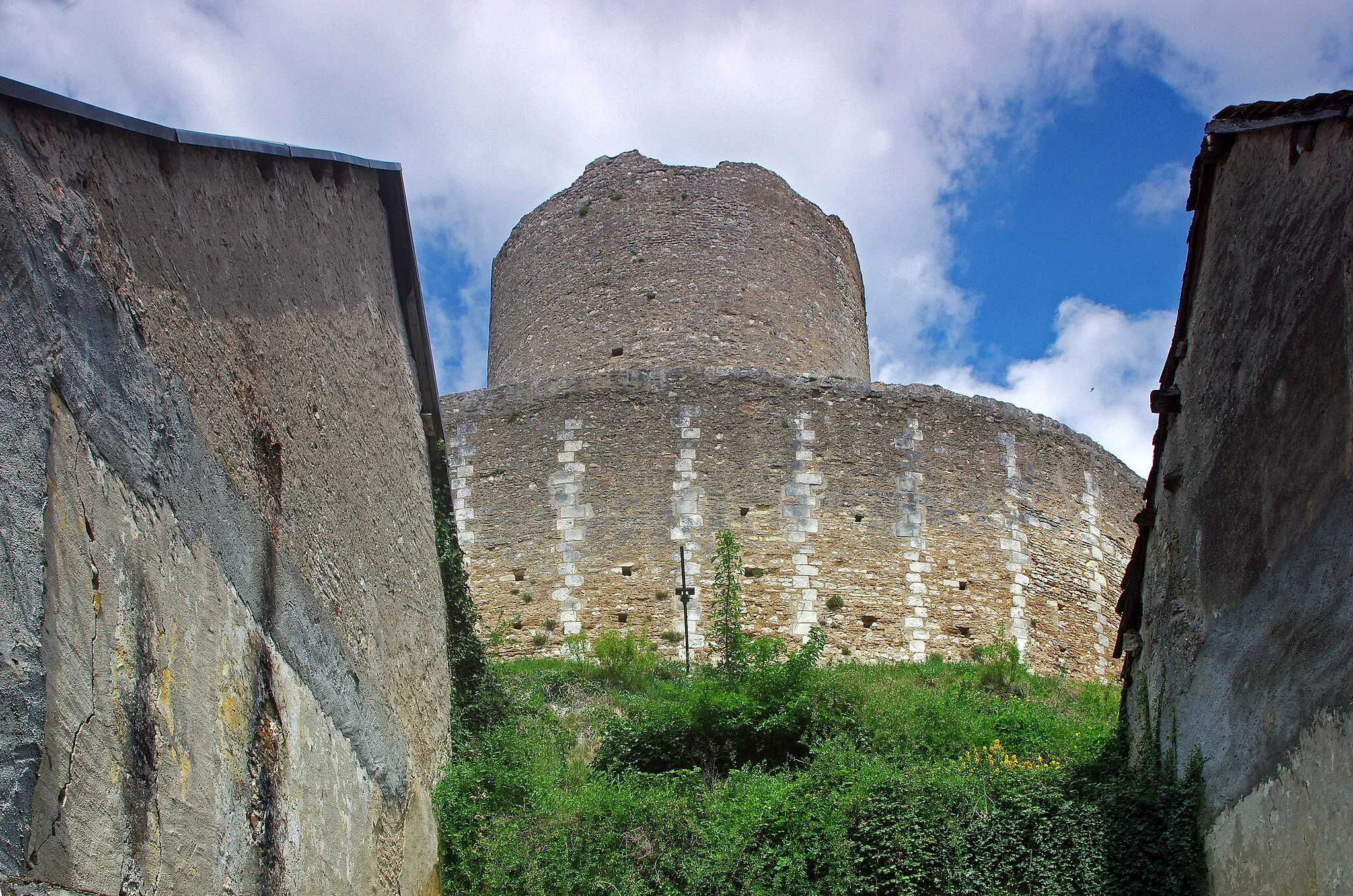 Photo showing: Châtillon-sur-Indre (Indre)
Le donjon (Tour de César) avec sa chemise.
Une chemise est un mur de protection, qui entoure une tour, un donjon ou un autre élément fortifié.
La Tour de César est le donjon d'un ancien château médiéval.
Ce genre de tour était un élément majeur de l'architecture militaire médiévale. On n'est ici pas très loin des limites de l'empire angevin, d'où la nécessité de surveiller les frontières.
Le donjon de Châtillon-sur-Indre est l'un des derniers vestiges d'un puissant château fort édifié sur ordre d'Henri II Plantagenêt vers 1160. Le château était en effet à la limite des domaines du roi de France et du roi d'Angleterre.
A la fin du XIIème siècle-début XIIIème, sous Philippe Auguste, le château entre dans le domaine du roi de France
En avril 1205, Philippe Auguste cédera le château, à titre provisoire, à Dreu de Mello, fils du connétable* de France Dreu III (ou IV) de Mello*.
A la mort, sans postérité, de Dreu de Mello, en 1249, les héritiers contesteront le retour du domaine dans le domaine royale. Après marchandage, le neveu de Dreu de Mello recevra 600 livres de rente pour renoncer à Châtillon et Loches. Ces 600 livres seront inscrites sur la recette des prévôtés et baillages*.
En septembre 1274, le roi Philippe III (Philippe le Hardi) donne le château à son Grand Chambellan*, Pierre de La Brosse*. Pierre de la Brosse qui ne possédera le château que jusqu'en 1278, pour cause de pendaison suite à une présumée trahison au profit d'Alphonse de Castille.
Pendant les XIIIème et XIVème siècles, le château  ne voit que le séjour temporaire et occasionnel du roi. Philippe III y séjournera du 26 a 30 novembre 1283; Philippe IV en mai 1289, août 1305 et février 1307; Jean II à l'hiver 1346.
Le château fait partie du duché de Touraine quand Louis d'Amboise en fait une prison en 1432.
La château quittera et retrouvera le domaine royal à plusieurs reprises. Au moment de la Révolution, la terre de Châtillon est dans la famille Amelot.
Tel qu'il se présente avec sa tour cylindrique qui culmine à 30 mètres, entourée d'un rempart de protection sur une motte calcaire rehaussée, c'est l'un des plus ancien de France. Au 19ème siècle, le château est découpé en parcelles. Le donjon et sa chemise seront donnés à la commune. La commune utilisera le donjon commle château d'eau en 1932.

Le connétable, "comes stabuli", comte de l'étable, est à l'origine chargé des écuries, donc des chevaux de guerre. Le connétable de France sera le chef des armées. Ici, il s'agit probablement de Dreu III (ou IV) de Mello, mort en 1218,  châtelain de Loches et Châtillon. Le châtelain n'est pas propriétaire du château, c'est souvent le commandant de la place. Son fils, Dreu de Mello, sera seigneur, donc propriétaire de Châtillon. Dreu III (ou IV) de Mello accompagna Philippe Auguste en Terre Sainte lors de la troisième croisade. Le roi le récompensera avec la charge de connétable et les châtellenies de Loches et Châtillon. Il décèdera le 3 mars 1218 à l'âge de 80 ans. Il aura trois enfants, Guillaume qui deviendra Guillaume Ier de Mello seigneur de Saint-Bris, Dreu de Mello qui sera seigneur de Loches et Châtillon, et Agnès qui sera mariée à Garnier III de Traînel, seigneur de Marigny. Prévôtés et bailliages sont des circonscriptions administratives et judiciaires. Le Grand Chambellan de France, très proche du roi, pourrait être comparé au premier ministre actuel. Pierre de la Brosse commence sa fortune comme barbier, et donc chirurgien, de Saint Louis. Le roi dut être content de ses services, puisqu'il en fit un châtelain et le nomma chambellan. Philippe, le fils du roi, le futur Philippe III dit le Hardi, fut également séduit par le personnage. Pierre de la Brosse accompagnera Saint Louis dans la huitième croisade, croisade où le roi trouvera la mort, de dysenterie, à Tunis (Lors de cette croisade, mourront également le fils aîné du roi et Isabelle d'Aragon). Philippe III succéda donc à son père et fit entière confiance à Pierre de la Brosse qu'il nomma Grand Chambellan de France. Pierre de la Brosse profita de cette promotion et de la confiance du roi pour placer toute sa famille en particulier grâce à des alliances matrimoniales avantageuses. Cette rapide ascension sociale d'un individu de petite noblesse (et non de basse extraction comme le prétendirent les jaloux), lui attira de nombreuses inimitiés chez les grands. Surtout, ceux-ci ne supportent pas d'être obligés de ramper à ses pieds pour bénéficier des libéralités royales. Le 21 août 1274, Philippe III épouse en secondes noces Marie de Brabant (sa première épouse, dont il aura quatre fils, Isabelle d'Aragon, était morte en Calabre, enceinte, au retour de la huitième croisade). Marie, prit ascendant sur le roi, ce qui causa bientôt de l'ombrage à l'ancien barbier. 
En mai 1276, le prince héritier Louis, issu du premier mariage, mourut subitement, à l'âge de 12 ou 13 ans. Des insinuations diffusées par Pierre de La Brosse, laissèrent entendre que le jeune Louis avait été empoisonné par sa belle-mère, Marie de Brabant, dans le dessein d'éliminer successivement les fils d'Isabelle d'Aragon et de promouvoir sa descendance. "En lan de grace mil CC.LXXVI. avint que Loys le premier filz le roy Phelippe mourut et fu empoisonné si comme aucuns dient. Le roy en fu en soupecçon, et ceste souspecçon mist en son cuer Pierre de la Broche, son maistre chambellenc".(Guillaume de Nangis, moine de Saint Denis mort en 1300 -"Gesta Philippi Tertia Francorum Regis")
La reine accuse à son tour le chambellan Pierre de la Brosse de manipulation. Pour se tirer d'affaire, il tenta, par l'intermédiaire de son cousin évêque de Bayeux, de suborner une béguine de Liège qui prétendait avoir des révélations à faire sur la mort du jeune Louis. L'évêque lui demanda de dire que la mort du jeune prince était due à la "clique brabançonne" qui entourait la reine. Mais l'évêque de Liège interrogea la béguine et révéla la supercherie. Toutefois, le roi hésitait encore à désavouer son favori et à innocenter sa femme. Il en fallait plus. Les "grands" trouvèrent : on l'accusa d'être à l'origine d'un revirement soudain du roi dans la campagne de Castille, suite à une manipulation. Pierre de la Brosse fut donc arrêté en janvier 1278 pour haute trahison. On l'éloigna de la capitale, à Janville(Eure-et-Loire), certainement pour que le roi ne puisse le sauver. Pierre de La Brosse fut jugé par les "grands", dont certains étaient d'ailleurs ses débiteurs,  et non par des gens de loi, et pendu le 30 juin 1278 au gibet de Montfaucon.

"(...) Quant les barons furent assemblez, Pierre fu tantost délivré au bourrel de Paris qui pent les larrons, à bon matin au soleil levant. Si le convoièrent au gibet, le duc de Bourgoingne; le duc de Breuban; le conte d'Artois, et plusieurs autres nobles barons. (...) Le bourrel lui mist la corde autour le col, et lui demanda s'il vouloit riens plus dire; et il dist que nennin; et tantost le bourel osta l'eschiele et le laissa aller entre les larrons."