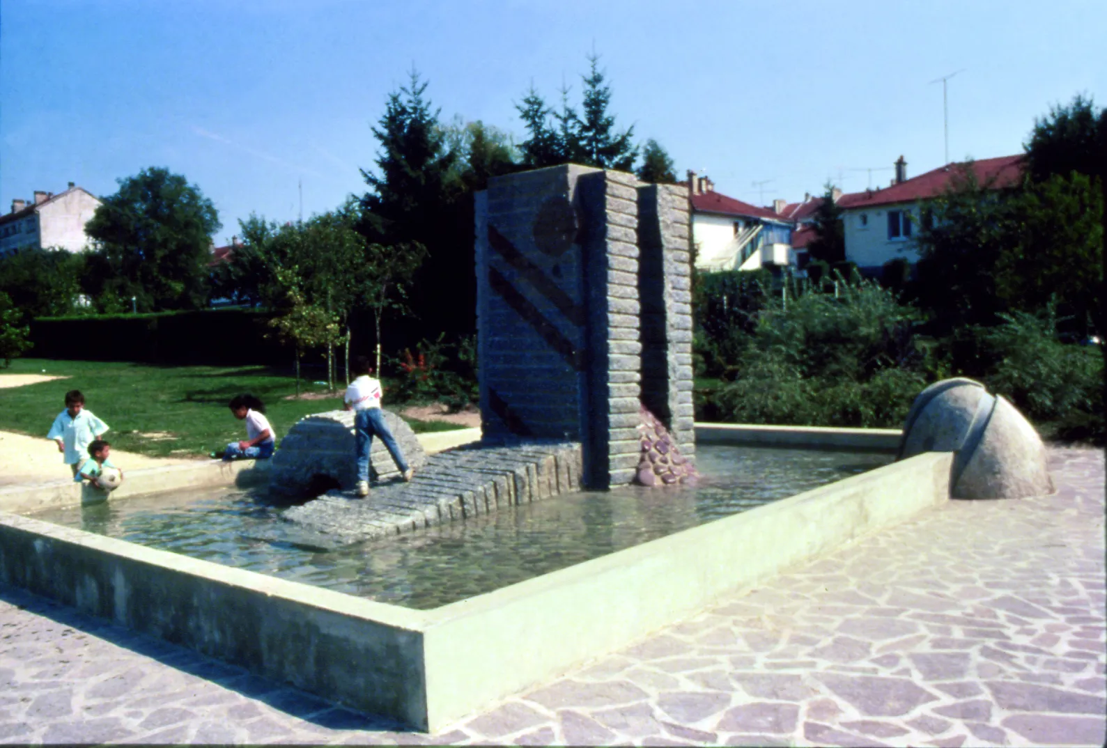Photo showing: Tetsuo Harada sculptor. Public commission, realization of “Fountain”, H 300, basins 800 x 600, made of grey granite encrusted with pink granite, pebbles. Totems H 300, placed in the City neighborhood des Vertes Voyes in Sainte Menehould, Champagne region. Organized by the Ministry of Education and the City of Sainte Menehould. The fountain will create the link between the old and new city neighborhood. The city of St. Ménéhould has a remarkable architectural know mixing brick with clear limestone. Located near the vocational school, the fountain is encrusted pink granite recalling the local style. Water flows from the top of granite columns and slid into the basin. Very shallow, it serves mainly to give more transparency to the work and to reflect the sky, clouds or the stars. The arrival of this sculpture has completely changed the use of this place that is now commemorative and well equipped. Competition "1%" of the Ministry of National Education and the municipality of Saint Ménéhould.