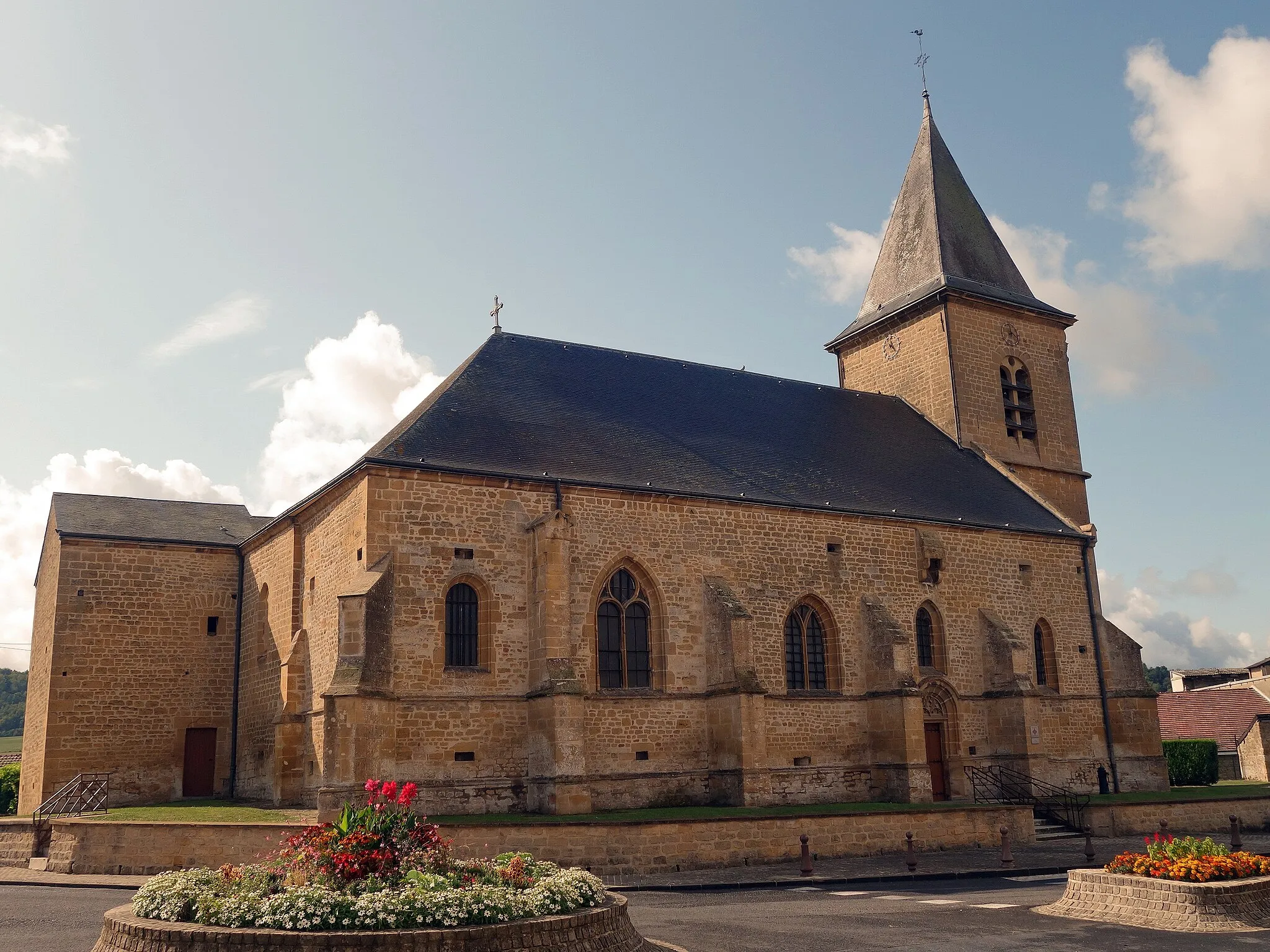 Photo showing: Aux abords de la Meuse, l'église Notre Dame du XVIe siècle possède une tour-porche et au niveau du chevet un bâtiment percé d'orifice de feux. De petites canonnières de fortifications sont encore visibles sur les bas-côtés.