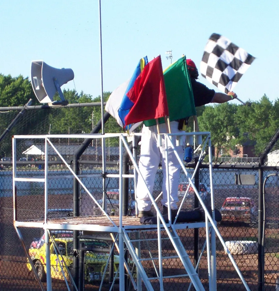 Photo showing: Looking at the flagman displaing the checkered flag at the Calumet County Racing Association stockcar races at the en:Calumet County, Wisconsin fairgrounds in Chilton, Wisconsin, USA. Note the complete set of racing flags (at least for American stockcar racing). The yellow flag is barely visible.