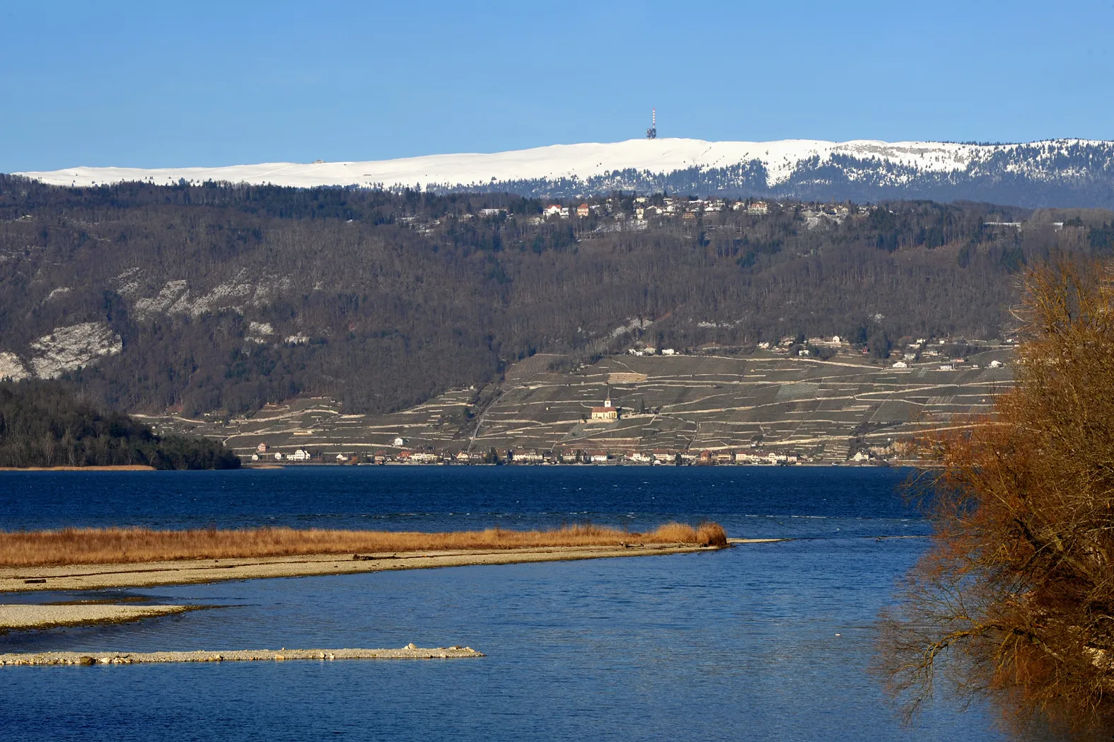 Photo showing: Estuary of the Aar into Lake Biel; Berne, Switzerland.
In the foreground the dam poured for the construction of the temporary pedestrian bridge. In the background Lake Biel the church of  Ligerz and the Chasseral.