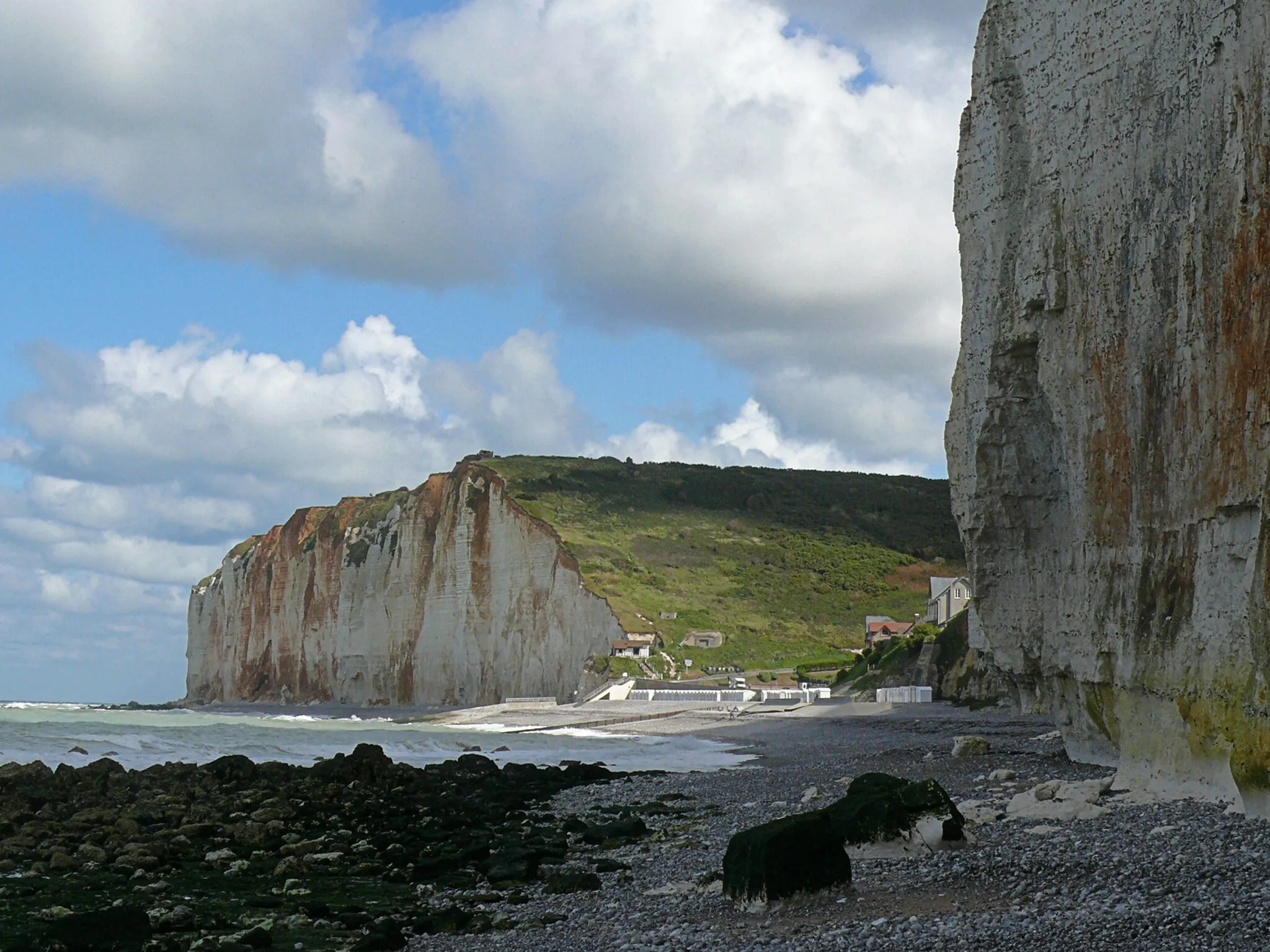 Photo showing: Photo of French landscape - a low view over the rocky bay with sun and light cloudy skies above the coast near Petit-Dalle in Normandy France, with a quiet sea and lively surf during late Summer of 2007 - on the background the cliffs on the northern side of the village.

French seascape photo - coast & landscape photography in France by Fons Heijnsbroek, photo in September 2007.