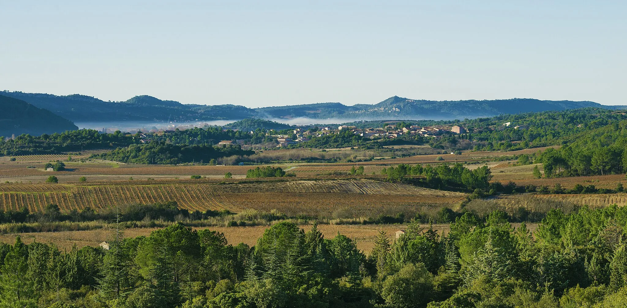 Photo showing: The village and the Southeastern part of the communal area seen from Northeast. Prades-sur-Vernazobre, Hérault, France. These vines are among those which produce the French wine Saint-Chinian.