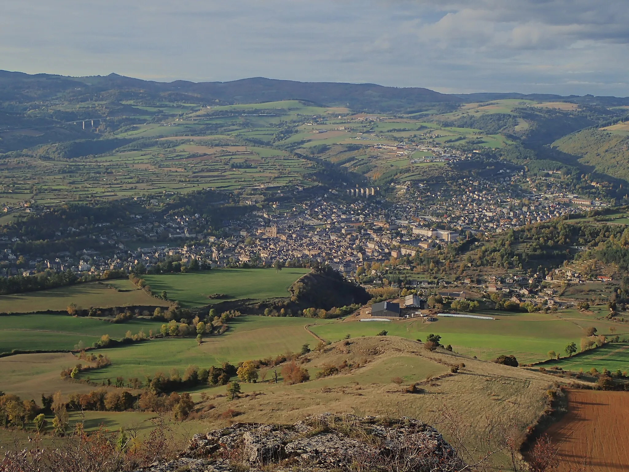 Photo showing: La ville de Marvejols (Lozère) vue du truc du Midi. A l'horizon, à gauche, les premiers sommets de l'Aubrac, en particulier le pic de Mus. On aperçoit également le pont autoroutier du Piou sur l'A75. Plus proche, on peut voir le pont de chemin de fer de Sénouard. Vue remarquable également sur le plateau de Lachamp, plateau calcaire cultivé dont les parcelles sont délimitées par des murs de pierres sèches. A l'extrême droite, on devine le début de la vallée de l'Enfer.