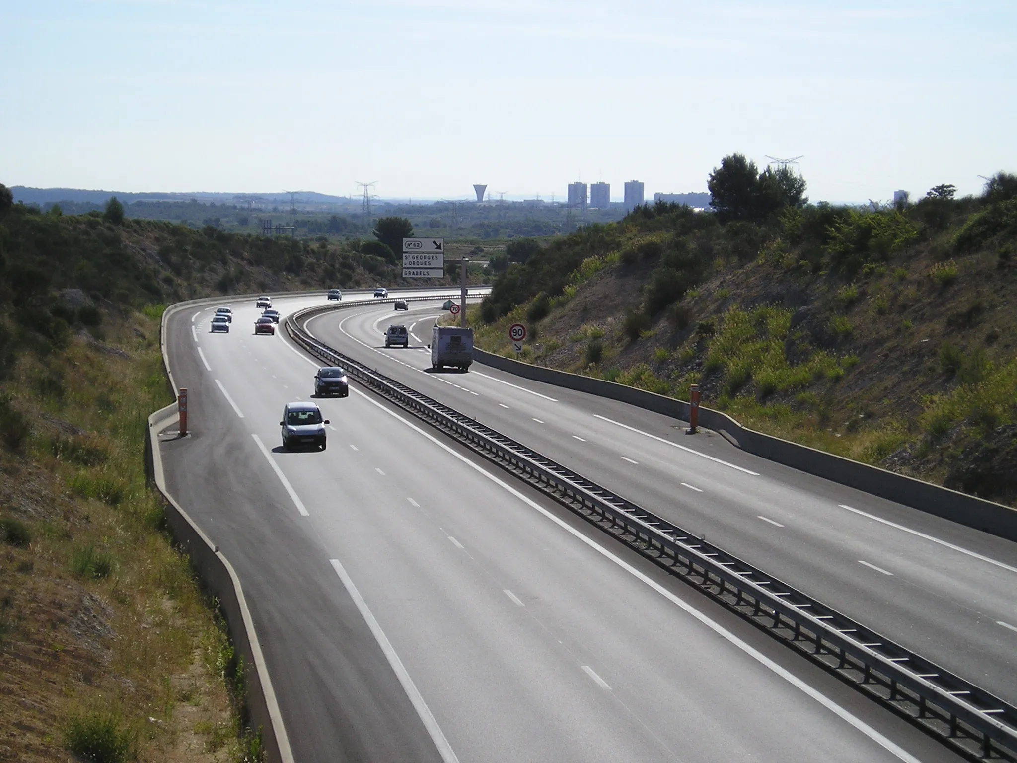 Photo showing: In Hérault, west of Montpellier, highway A750 viewed from the bridge on the D102 road next to Bel-Air and exit #62 (on Saint-Georges-d'Orques territory). In the background, the northern part of Montpellier area of La Paillade (water reservoir and the three towers of residential "Tritons" estate).