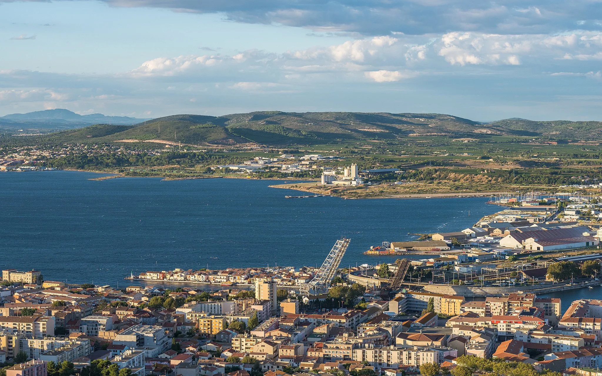 Photo showing: The Eastern end of the Étang de Thau from the Mount Saint-Clair in Sète, Hérault, France. In the foreground, a part of the town of Sète with the Pointe Courte Neighbourhood, the Maréchal Foch and Sadi-Carnot Bridges (the both are bascule bridges, here in open positions) over the Canal of Sète, and the train station. In background, at right a part of the commune of Frontignan, at left a part of the commune of Balaruc-les-Bains and behind the both the La Gardiole Mountain.