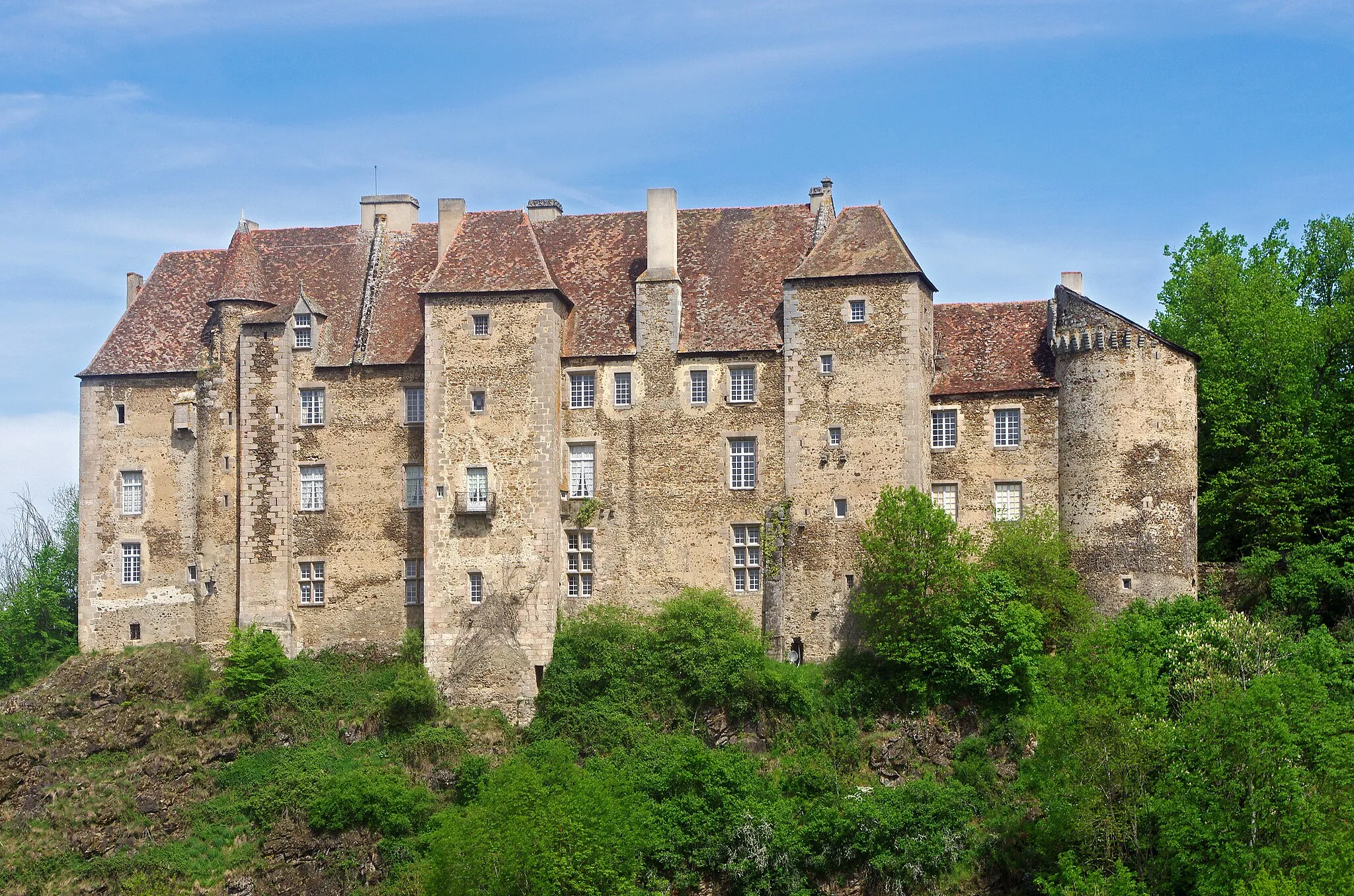 Photo showing: Boussac (Creuse).
Le château de Boussac.
Le château domine la vallée de la Petite-Creuse.
Le château fut érigé au 12éme siècle et en partie détruit par les anglais pendant la guerre de Cent Ans.
Au 15ème siècle, Jean Ier de Brosse, maréchal de France et compagnon de Jeanne d'Arc fit reconstruire le château. Le château a été remanié aux 16éme et 17éme siècles.
George sand résida dans le château à deux reprises, pour fuir une épidémie de variole à Nohant* et durant la guerre de 1870.
George Sand décrit le château de Boussac, dans son premier roman champêtre Jeanne*.

"La ville de Boussac, formant, avec le bourg du même nom, une population de dix-huit à dix-neuf cents âmes, peut être considérée comme une des plus chétives et des plus laides sous-préfectures du centre. Ce n’est pourtant pas l’avis du narrateur de cette histoire. Jeté sur des collines abruptes, le long de la Petite-Creuse, au confluent d’un autre ruisseau rapide, Boussac offre un assemblage de maisons, de rochers, de torrents, de rues mal agencées, et de chemins escarpés, qui lui donnent une physionomie très pittoresque.
(...)
Boussac a le bon goût de se lier si bien au sol, qu’on y peut faire une belle étude de paysage à chaque pas en pleine rue. Mais il se passera bien du temps avant que les citadins de nos provinces comprennent que la végétation, la perspective, le mouvement du terrain, le bruit du torrent et les masses granitiques font partie essentielle de la beauté des villes qui ne peuvent prétendre à briller par leurs monuments. Il y a cependant un monument à Boussac, c’est le château d’origine romaine que Jean de Brosse, le fameux maréchal de Boussac, fit reconstruire en 1400 à la mode de son temps. Il est irrégulier, gracieux et coquet dans sa simplicité. Cependant les murs ont dix pieds d’épaisseur, et dès qu’on franchit le seuil, on trouve que l’intérieur a la mauvaise mine de tous ces grands brigands du moyen âge que nous voyons dans nos provinces dresser encore fièrement la tête sur toutes les hauteurs.
Ce château est moitié à la ville et moitié à la campagne. La cour et la façade armoriée regardent la ville ; mais l’autre face plonge avec le roc perpendiculaire qui la porte jusqu’au lit de la Petite-Creuse, et domine un site admirable, le cours sinueux du torrent encaissé dans les rochers, d’immenses prairies semées de châtaigniers, un vaste horizon, une profondeur à donner des vertiges. Le château, avec ses fortifications, ferme la ville de ce côté-là."
(George Sand - Jeanne)

Les Prussiens envahissent Paris le 19 septembre 1870. Pendant la même période, la variole se répand à Nohant. Son fils et ses deux petites-filles étaient déjà tombé gravement malade de la variole charbonneuse au début de l’année. Son fils, Maurice,  était resté dans un état critique pendant seize jours. Pour éviter tout nouveau risque, la famille prend la décision de se réfugier à Boussac. (Correspondance, Nohant le 15 septembre et Journal 16.9.1870)
Jeanne,  jeune bergère de la Marche, est engagée comme servante à la petite ville voisine de Boussac. Trois hommes la désirent: l'avocat Marsillat, l'aristocrate Guillaume de Boussac et sir Arthur, un riche Anglais. Sir Arthur souhaite épouser Jeanne, mais elle ne peut accepter en raison d'un vœu qu'elle a fait.  Pressée par Marsillat, Jeanne, pour lui échapper, se jette par une fenêtre. Jeanne représente évidemment le Peuple face à l'aristocratie, la bourgeoisie, les notables, la richesse. Chacun tente de séduire Jeanne à sa façon.
Par exemple, l'avocat Marsillat s'adresse à l'aristocrate Guillaume de la Brosse :"Car il entre dans les idées de votre caste de perpétuer l’ignorance chez le pauvre, afin d’y perpétuer la soumission. Aussi admirez vous, en poètes, que vous prétendez être, le merveilleux qui remplit ces pauvres cervelles ; et vous ne faites qu'entretenir, par la dévotion, par la protection accordée aux images miraculeuses, aux pèlerinages, et autres niaiseries, la folie de nos pauvres villageois."