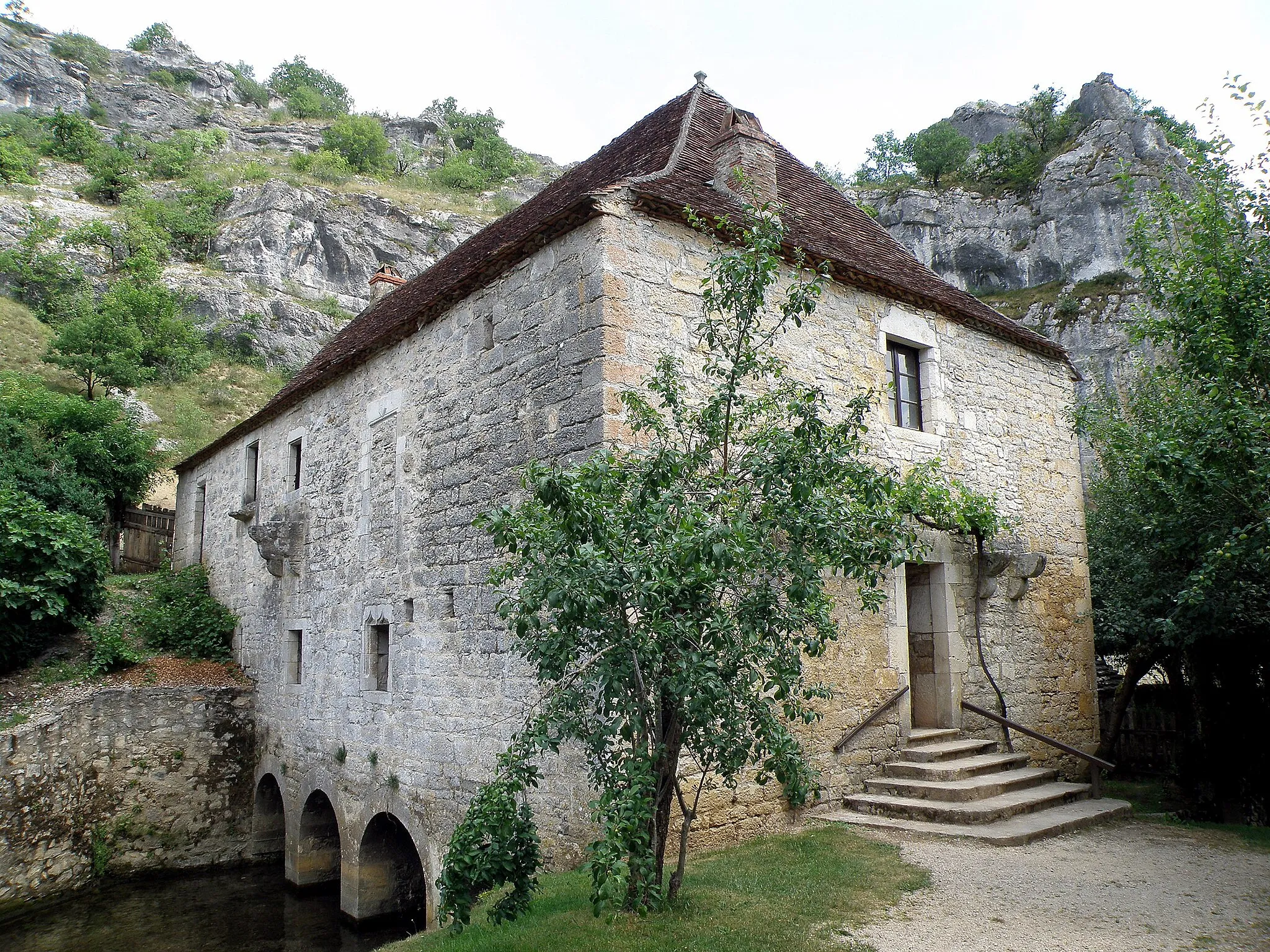 Photo showing: Calès, commune du département du Lot (région Midi-Pyrénées, France). Moulin à eau de Cougnaguet (ou de Cognaguet ― selon la Base Mérimée ― ou de Caugnaguet ― graphie retenue par l’IGN), sis sur la rive droite de la rivière Ouysse, affluent gauche de la Dordogne. Façade nord (à gauche) et ouest (à droite, avec vestiges de bretèche défensive) du moulin ; bief de fuite (en bas à gauche).