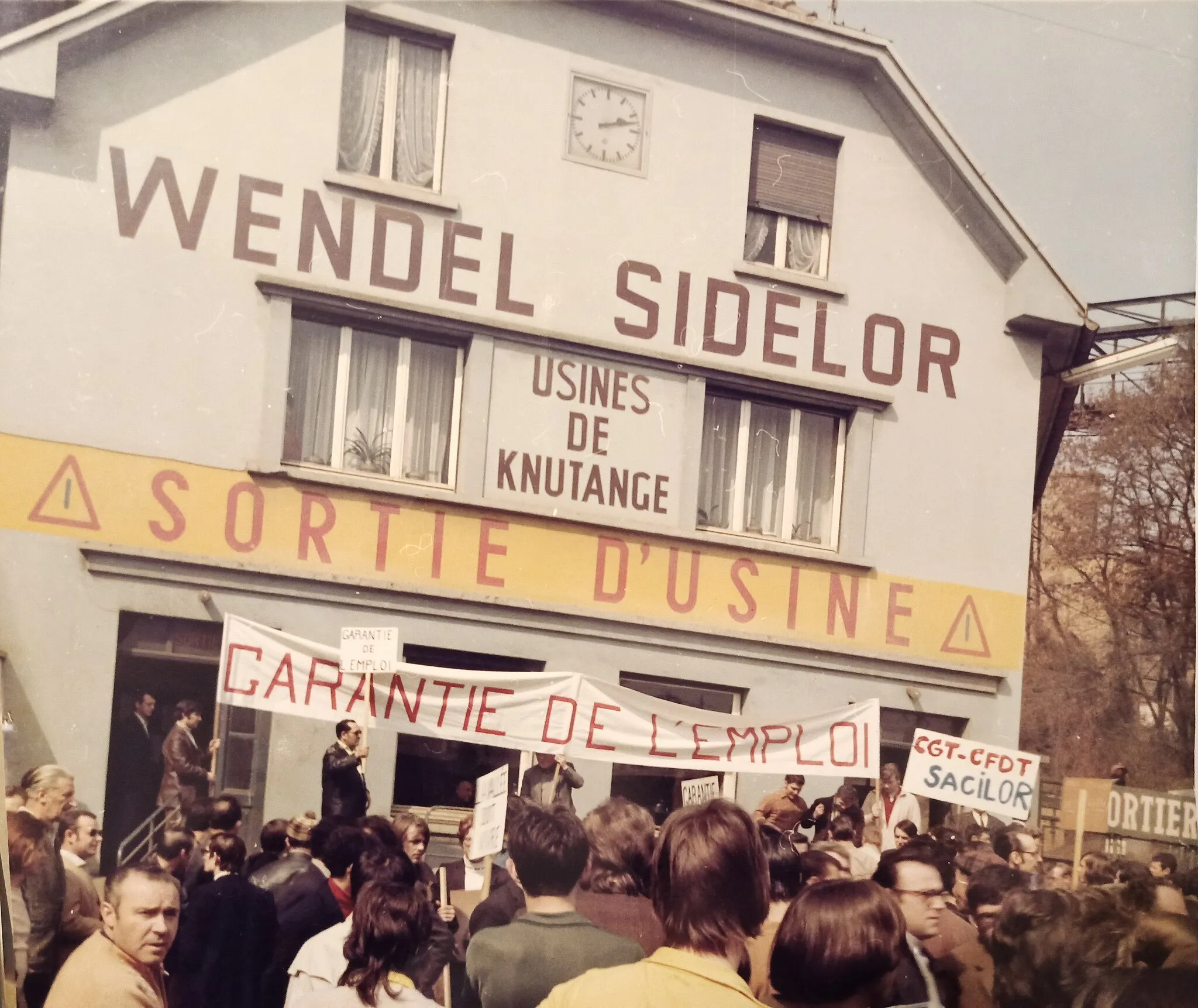 Photo showing: Manifestation au portier de l'usine du bas en 1971. Le batiment du portier porte l'inscription "wendel sidelor- usines de Knutange". Wendel Sidelor a absorbé la Société Mosellane de Sidérurgie, elle même étant le fruit de la fusion S.M.K.-U.C.P.M.I