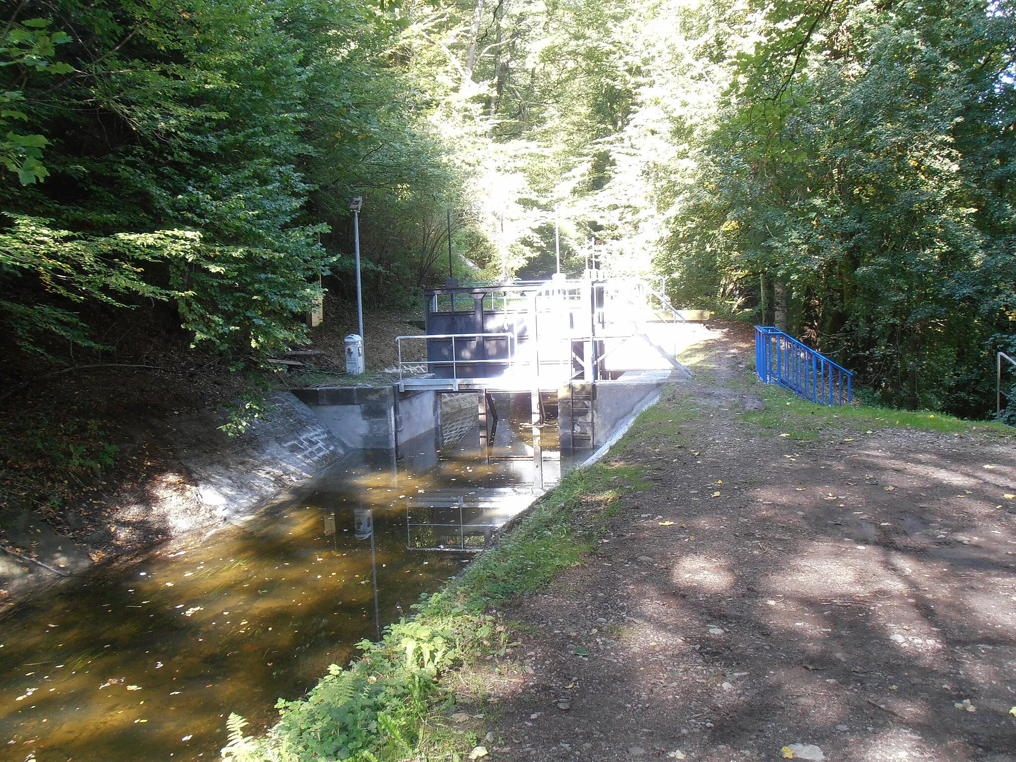 Photo showing: Vosges, Moraine de Noirgueux sur les communes de Saint-Nabord, Saint-Étienne-lès-Remiremont, Éloyes, Remiremont : écluse sur le canal de Bouzey sur le sentier de la "moraine de Noirgueux".
Les travaux d'édification de la rigole et de ses ouvrages entre la prise d'eau de Remiremont et Arches, sur 19,467 km, ont débuté en 1882 et ont été terminés en 1887 (Extrait de « Le canal de l'Est, branche sud » par M. Boulet, ingénieur en chef des Ponts et Chaussées du département des Vosges, Science et industrie, 1935).

La rigole principale débute à Saint-Etienne-lès-Remiremont. Une partie de l'eau de la Moselle est déviée sur la rigole, où elle s'écoule par gravité sur plus de 45 kilomètres jusqu'au réservoir de Bouzey. De là elle se déverse dans le canal des Vosges et sert aux besoins de la navigation, essentiellement des plaisanciers (Le canal d'alimentation de Bouzey, panneau de signalétique sur le sentier pédagogique de la moraine de Noirgueux)