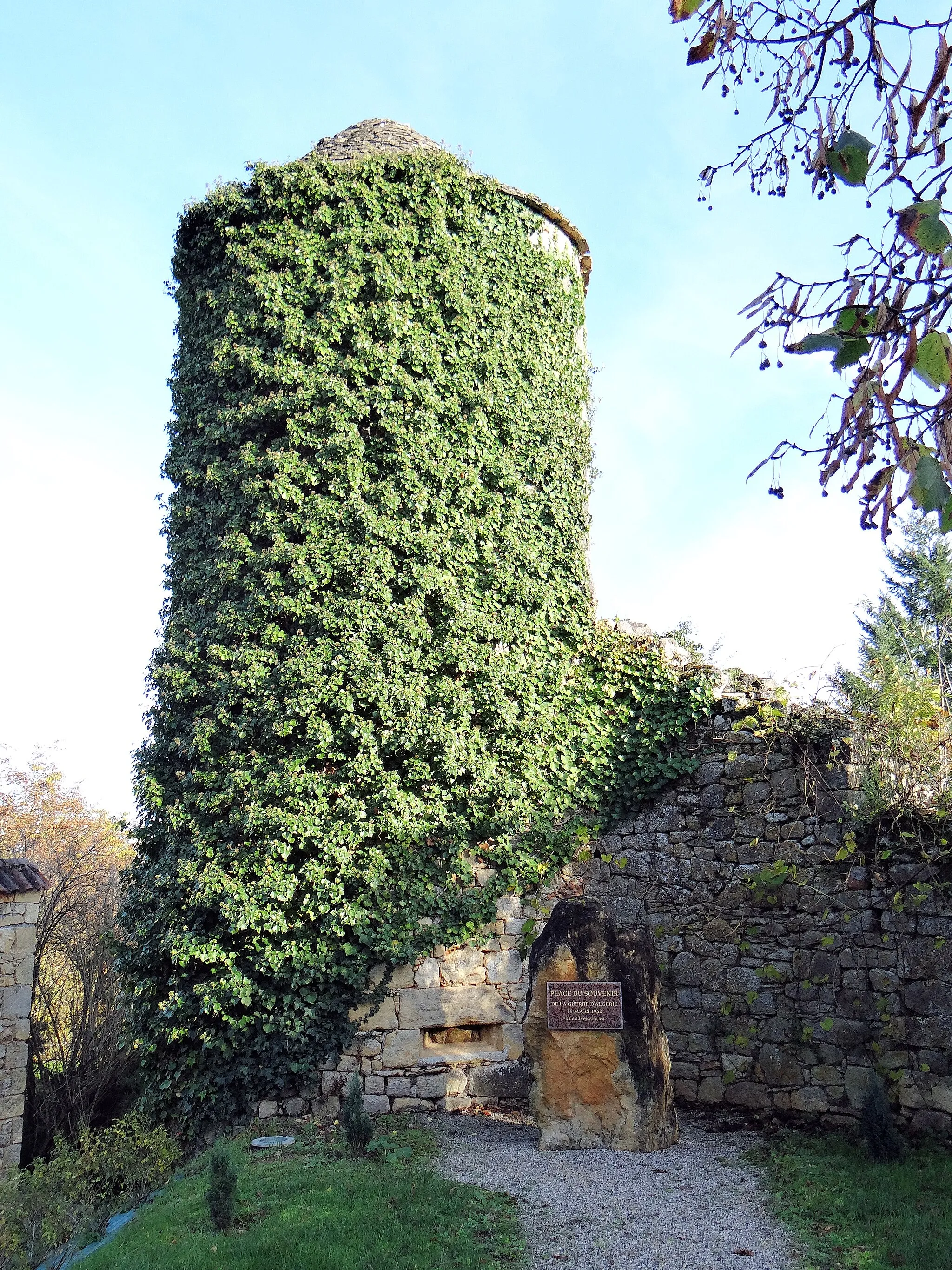 Photo showing: Château de Milhac - Une tour de l'enceinte du château, derrière un monument du souvenir de la guerre d'Algérie