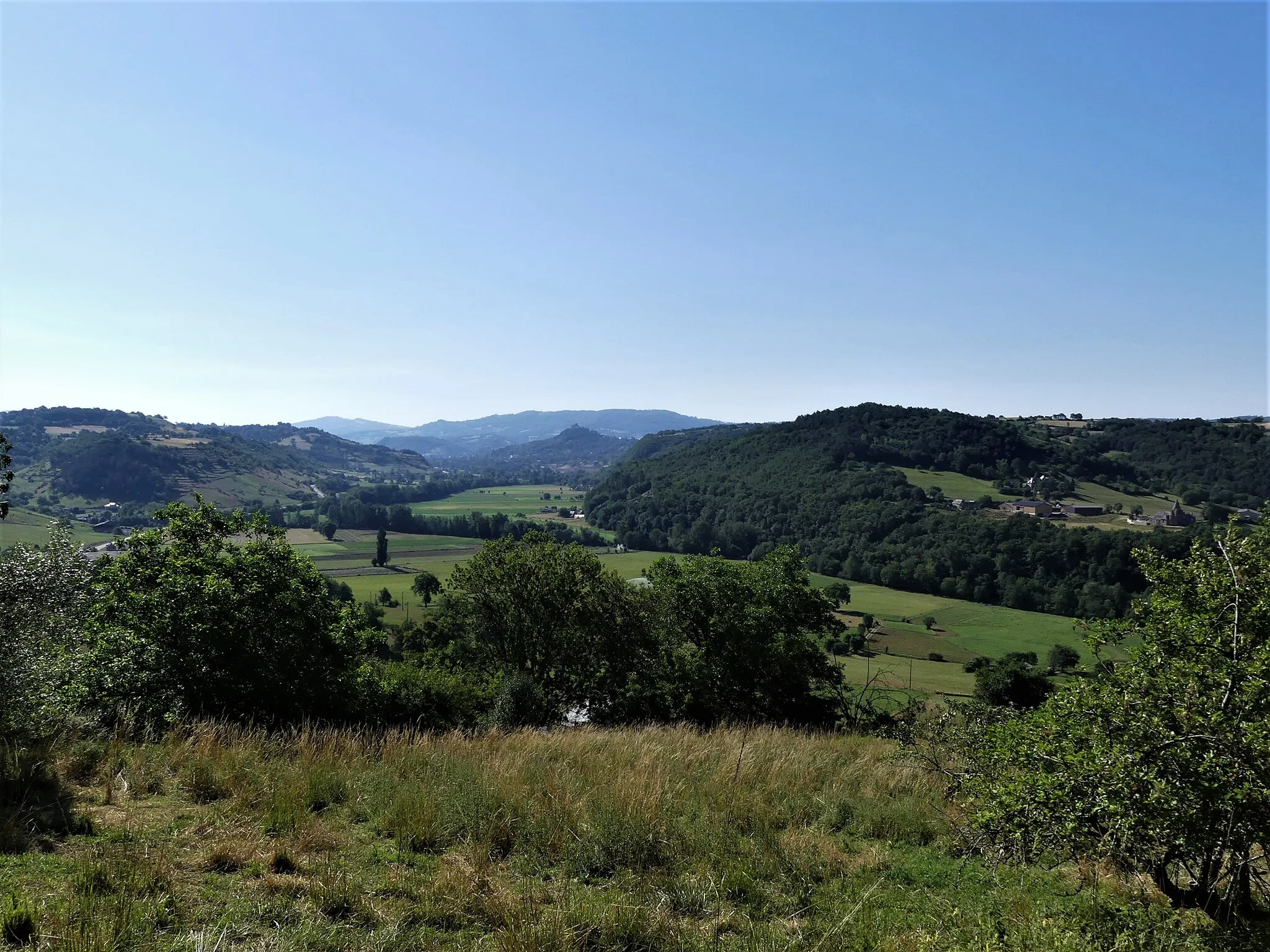 Photo showing: La vallée du Lot vue depuis Vinnac, Estaing, Aveyron, France. Vue prise en direction de l'amont. Sur la gauche, commune de Coubisou ; sur la droite communes de Sébrazac et Bessuéjouls ; au fond, Espalion avec la silhouette du château de Calmont d'Olt sur sa colline.