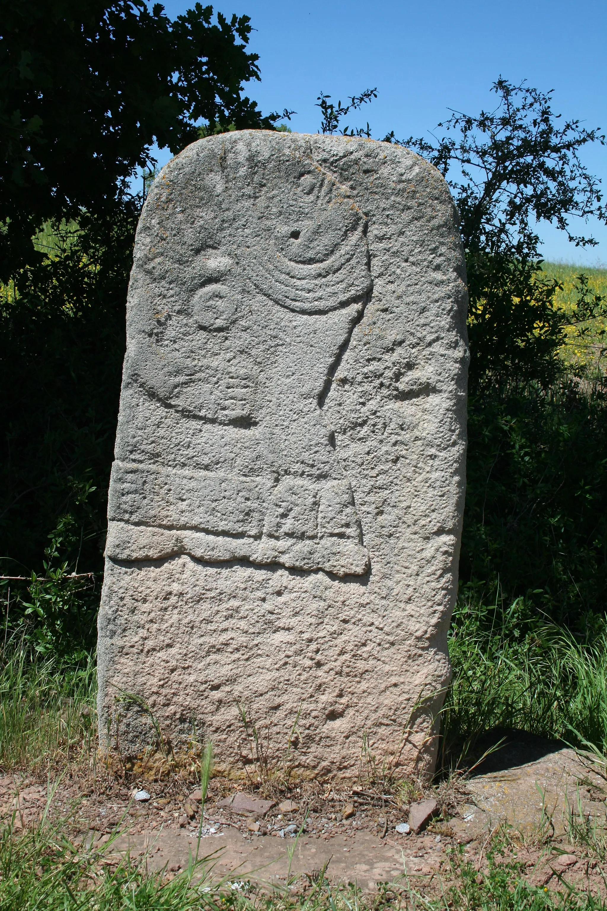 Photo showing: Combret (Aveyron) - copie en grès de la statue-menhir de Serres découverte en 1996 au lieu-dit Luchau près de la ferme de Serres. Il s'agit d'une statue-menhir féminine. On voit : des tatouages de par et d'autre du nez, un grand collier à cinq rangs, un sein au dessus du bras droit replié,  une large ceinture.