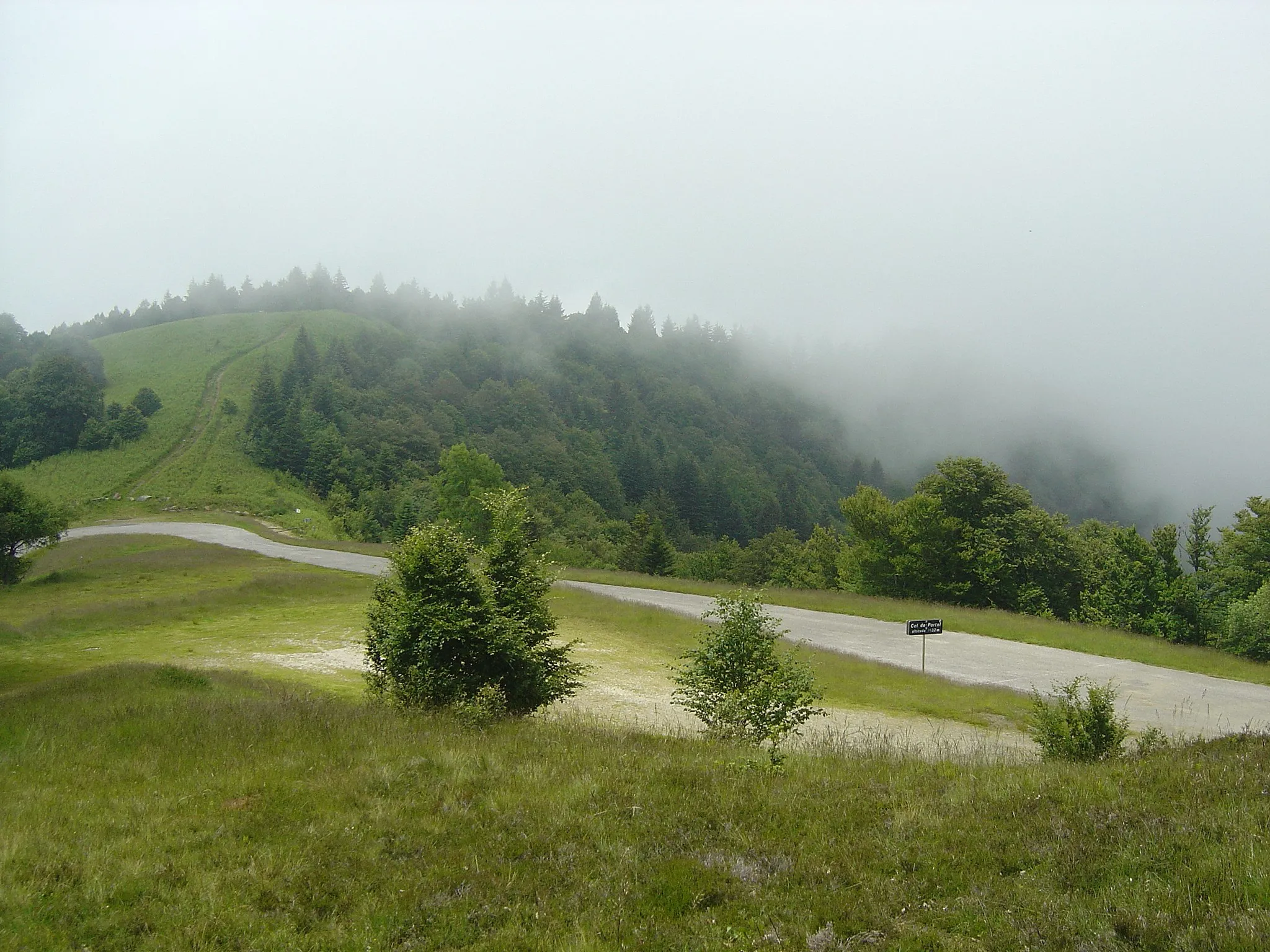 Photo showing: Le col de Portel et plus loin le sommet de Portel (1465m). Le col de Portel est indiqué à 1432m d'altitude alors qu'en fait cette altitude est celle de la dernière épingle au fond et que cela continue de grimper un peu jusqu'au panneau.